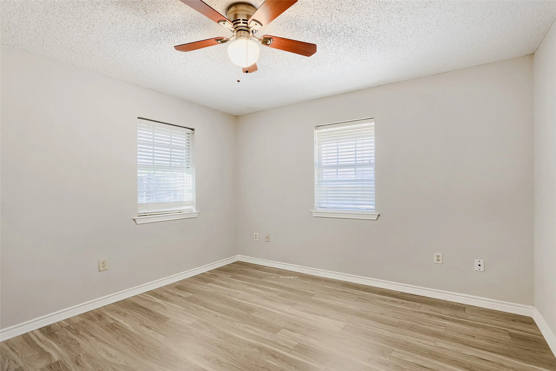 Wood-finish flooring, two windows with blinds, ceiling fan with integrated lighting, and neutral wall paint