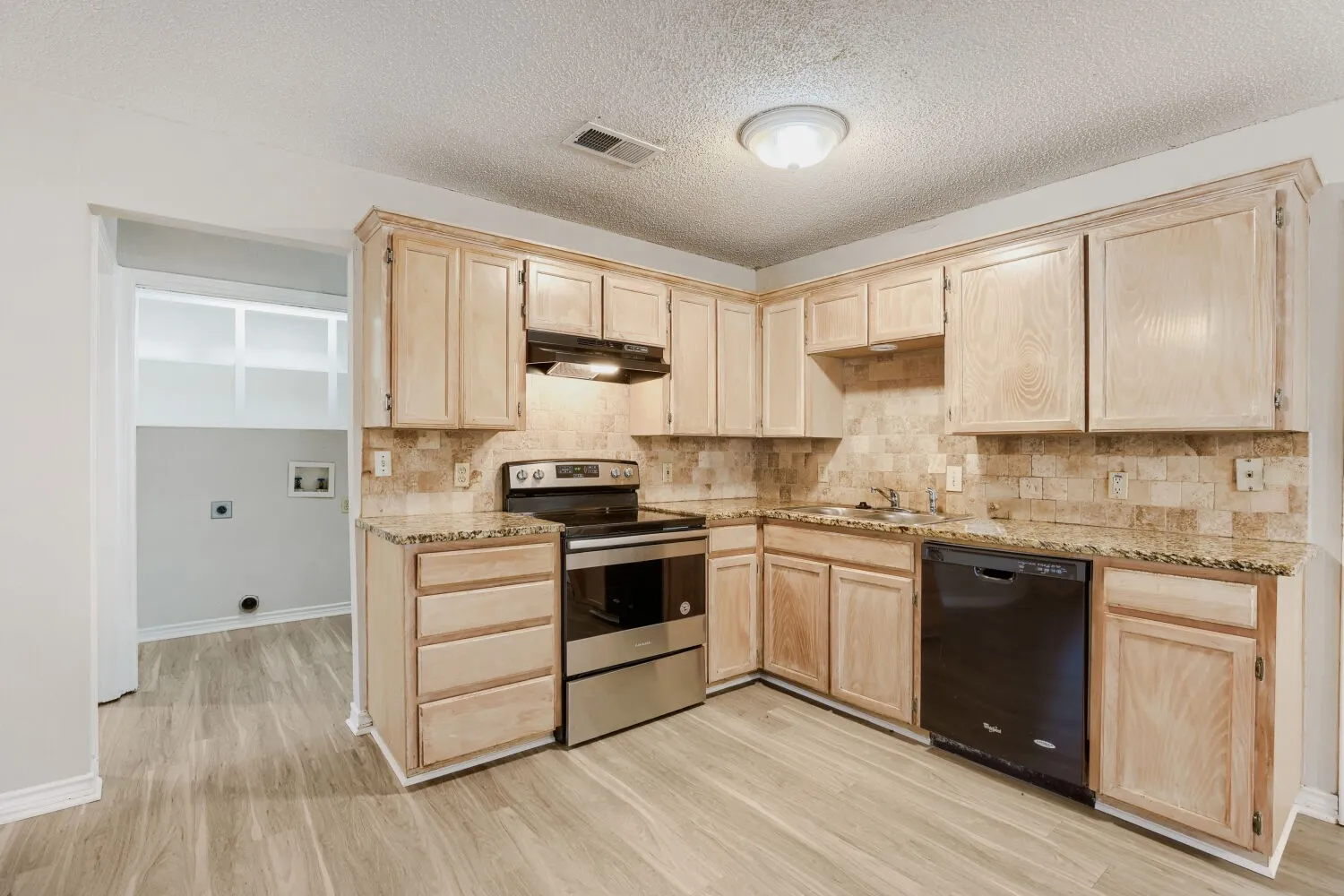 Kitchen featuring wood-finish cabinetry, stone countertops, a tile backsplash, and stainless steel and black appliances