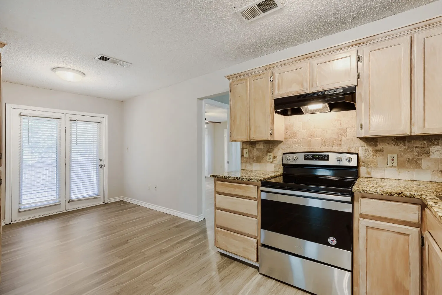 Wood-finish flooring, light-toned cabinetry, stainless steel range, patterned stone-look countertops, and a tiled​​‌​​​​‌​​‌‌​‌‌​​​‌‌​‌​‌​‌​​​‌​​ backsplash