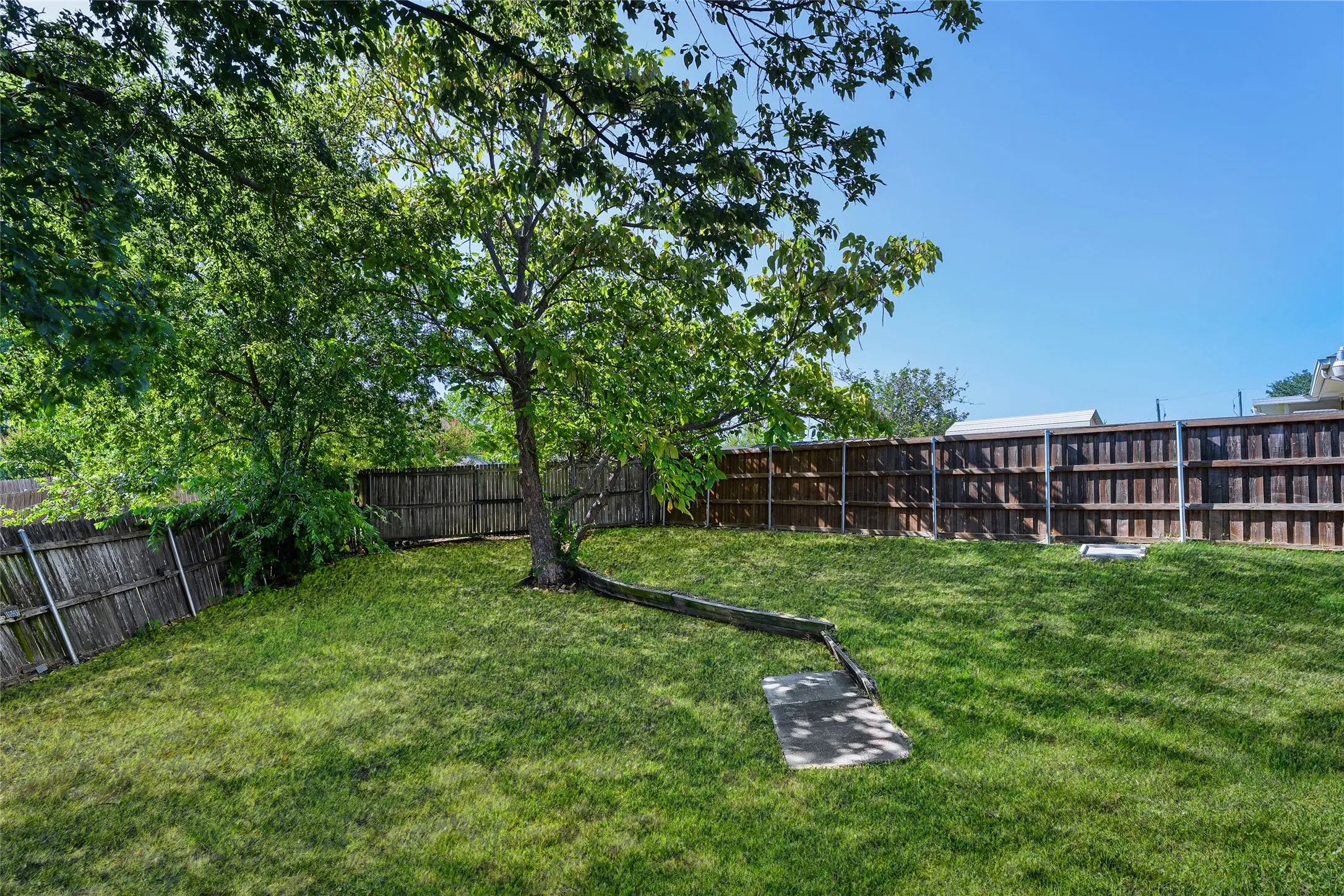 Expansive backyard featuring a lush lawn, mature trees, and privacy fencing