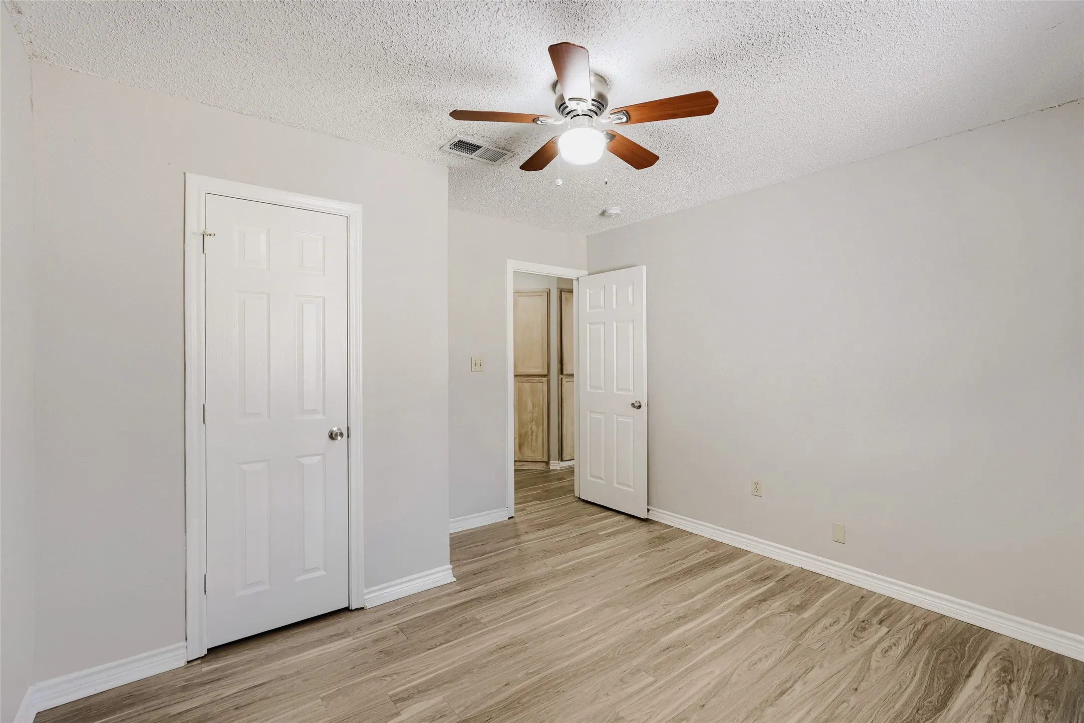Wood-finish flooring, ceiling fan with integrated lighting, white paneled doors, and light-toned wall finishes