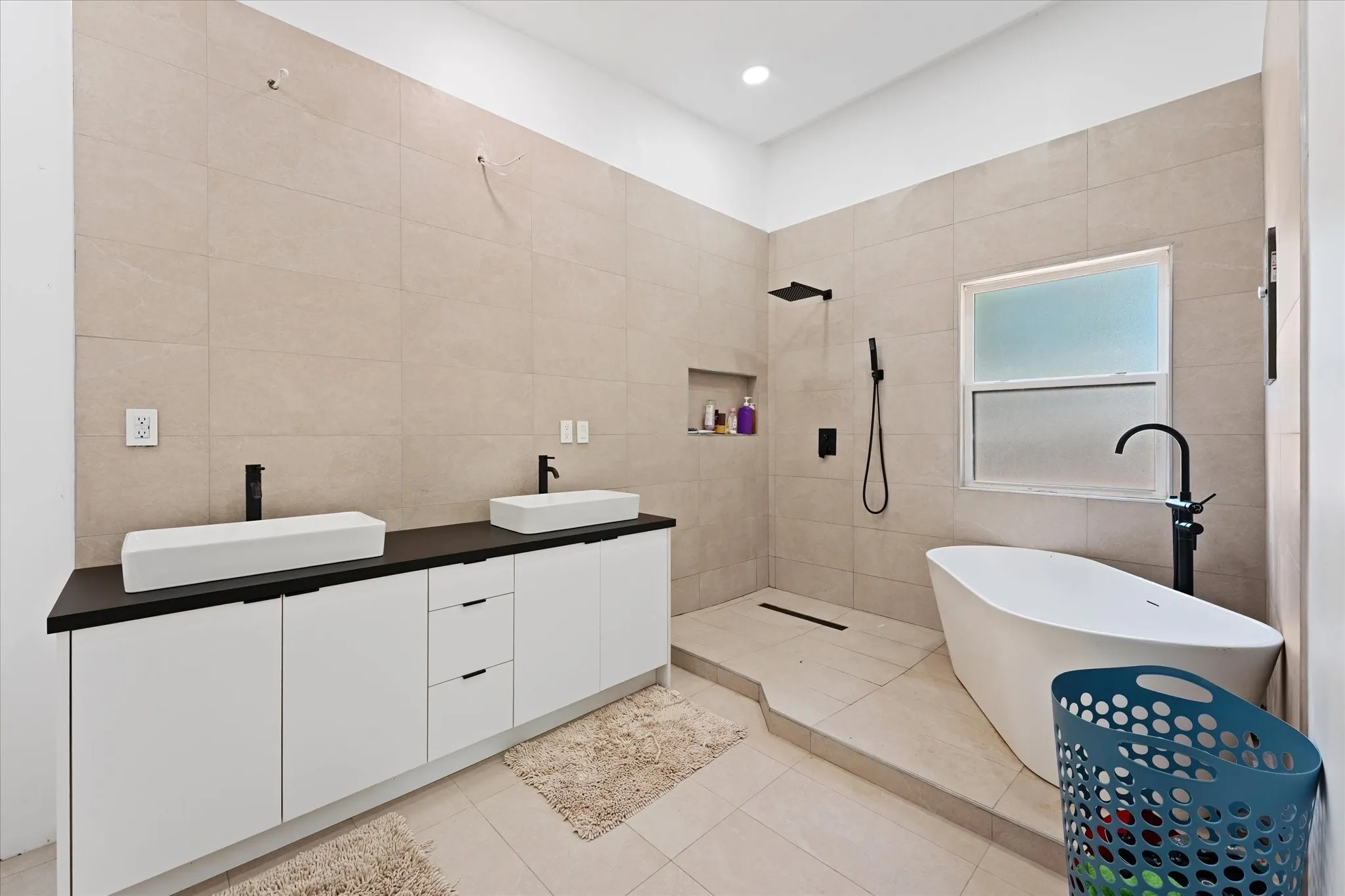 Dual rectangular vessel sinks, extensive vanity storage, walk-in shower with built-in niche, matte black fixtures, and a freestanding soaking tub