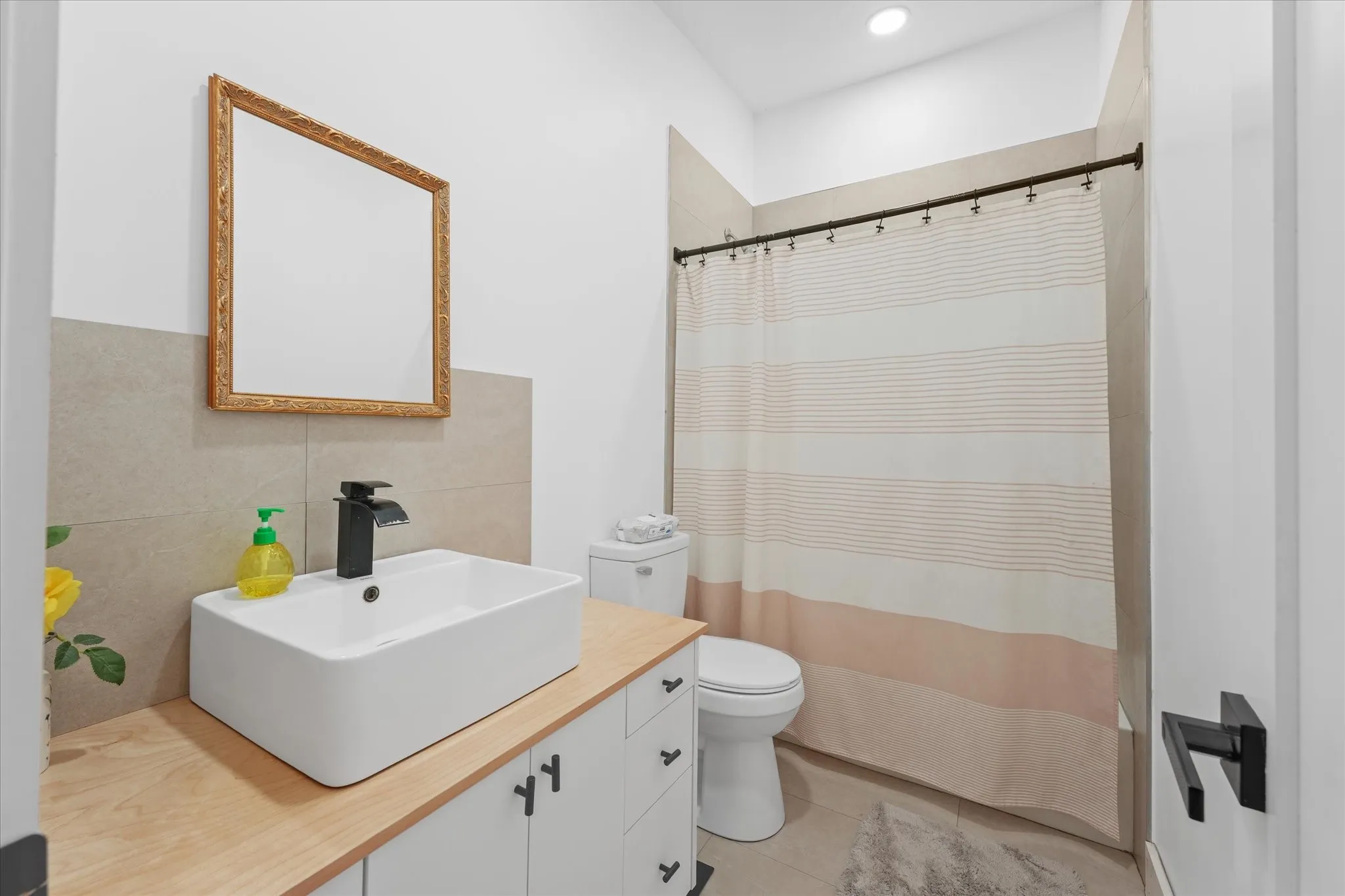 Bathroom featuring a vessel sink, wood-finish countertop, white cabinetry with dark hardware, and a tiled shower surround