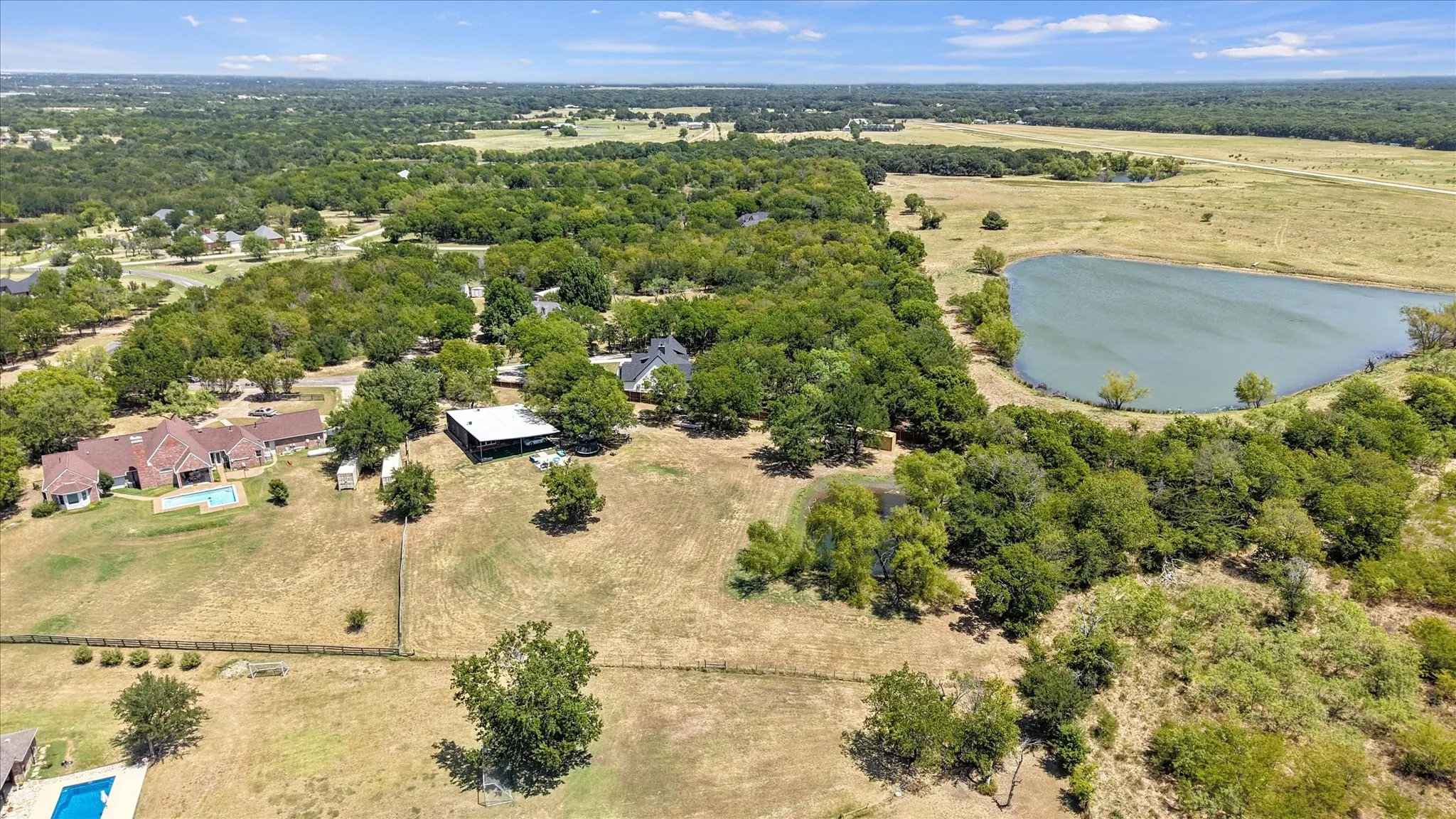 Expansive property featuring a private pond, abundant mature trees, open land, and a residential structure with an outdoor pool