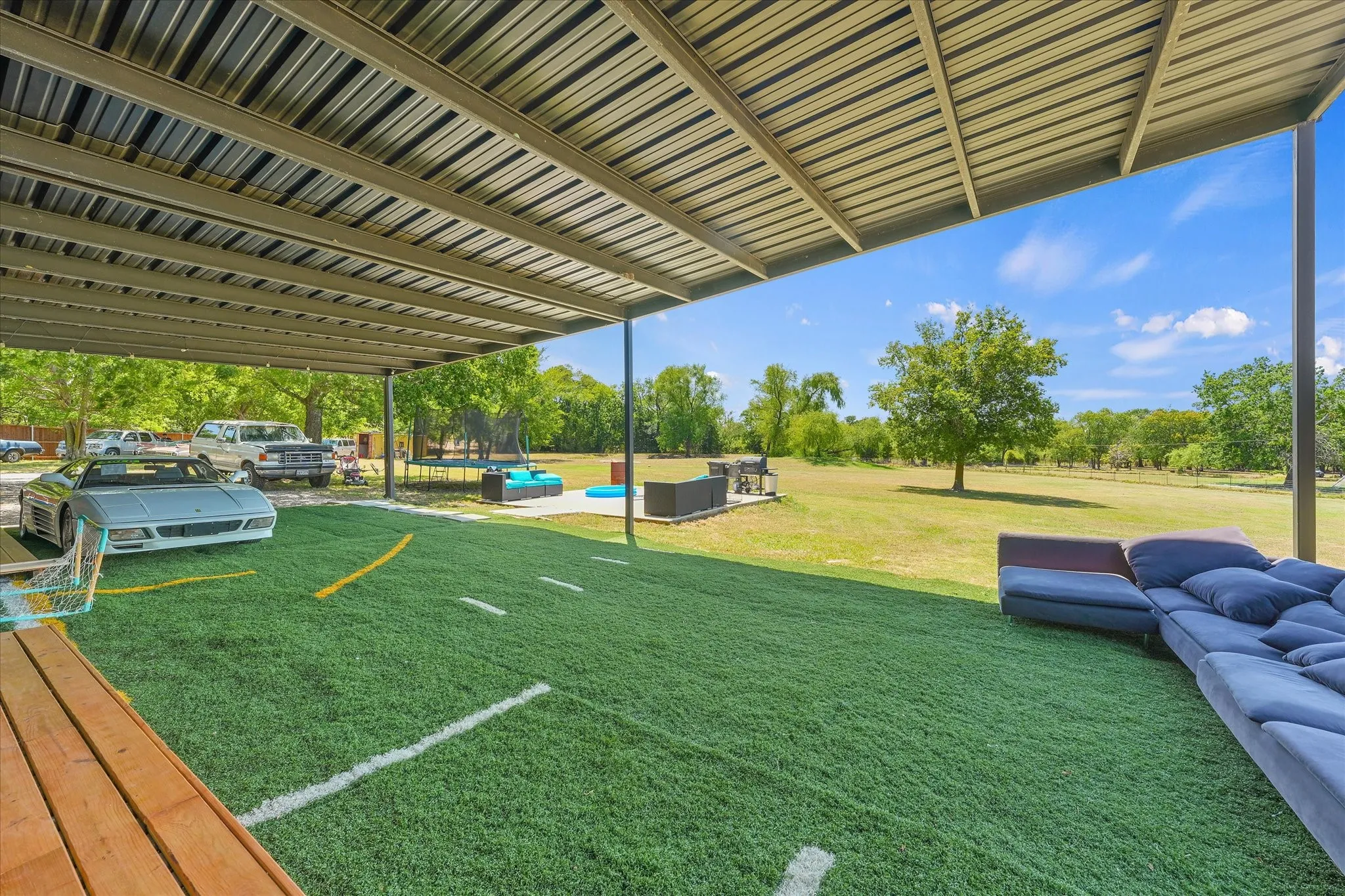 Expansive covered patio featuring artificial turf, a metal roof structure, and open-air access to a large grass area