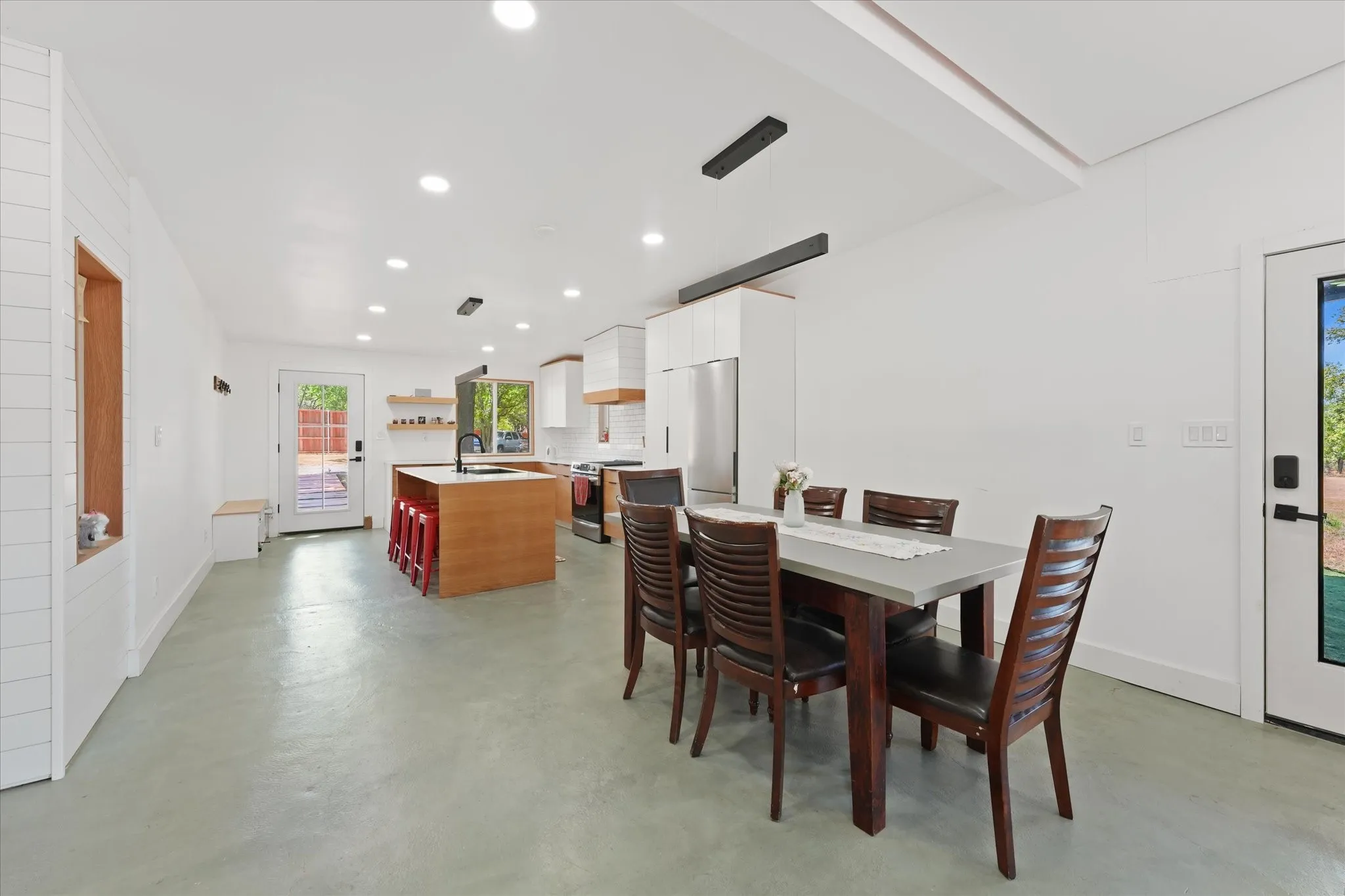 Open-concept living space featuring light-toned flooring, recessed lighting, and a kitchen island with a dark-toned sink