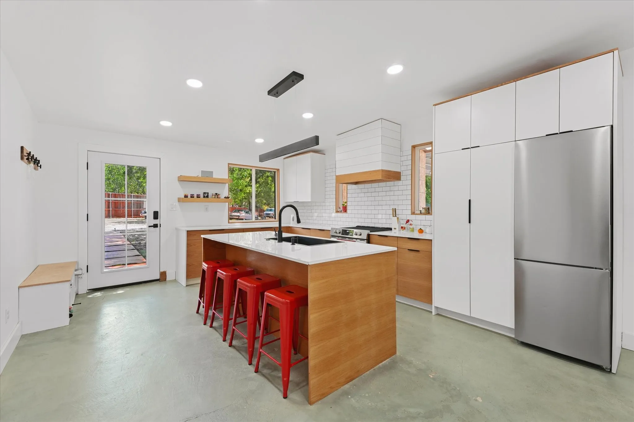 Modern kitchen featuring a central island with white countertop, stainless steel refrigerator, white subway tile backsplash, and recessed lighting