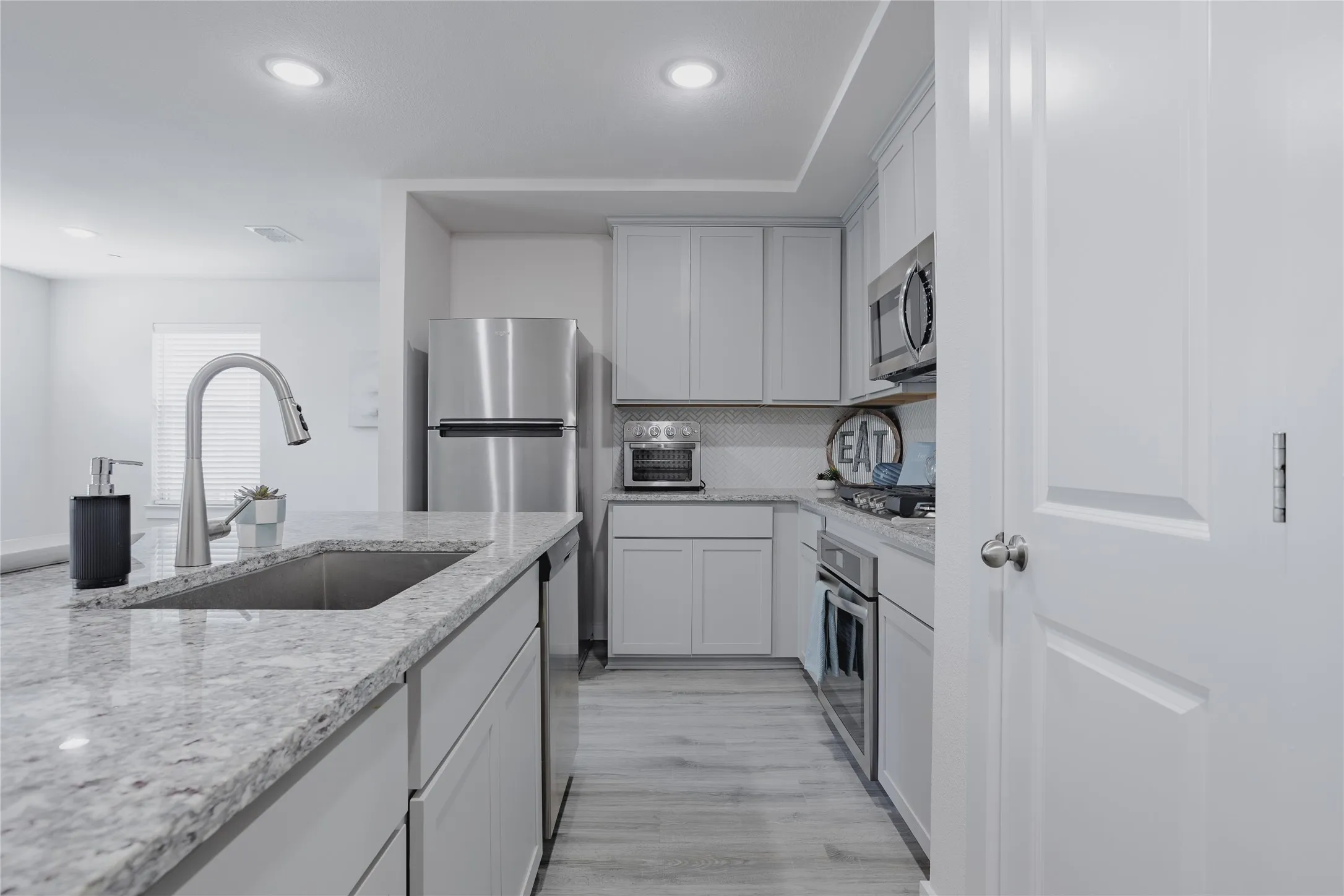 Kitchen featuring light-toned cabinetry, stainless steel appliances, recessed lighting, wood-finish flooring, and light-toned countertops