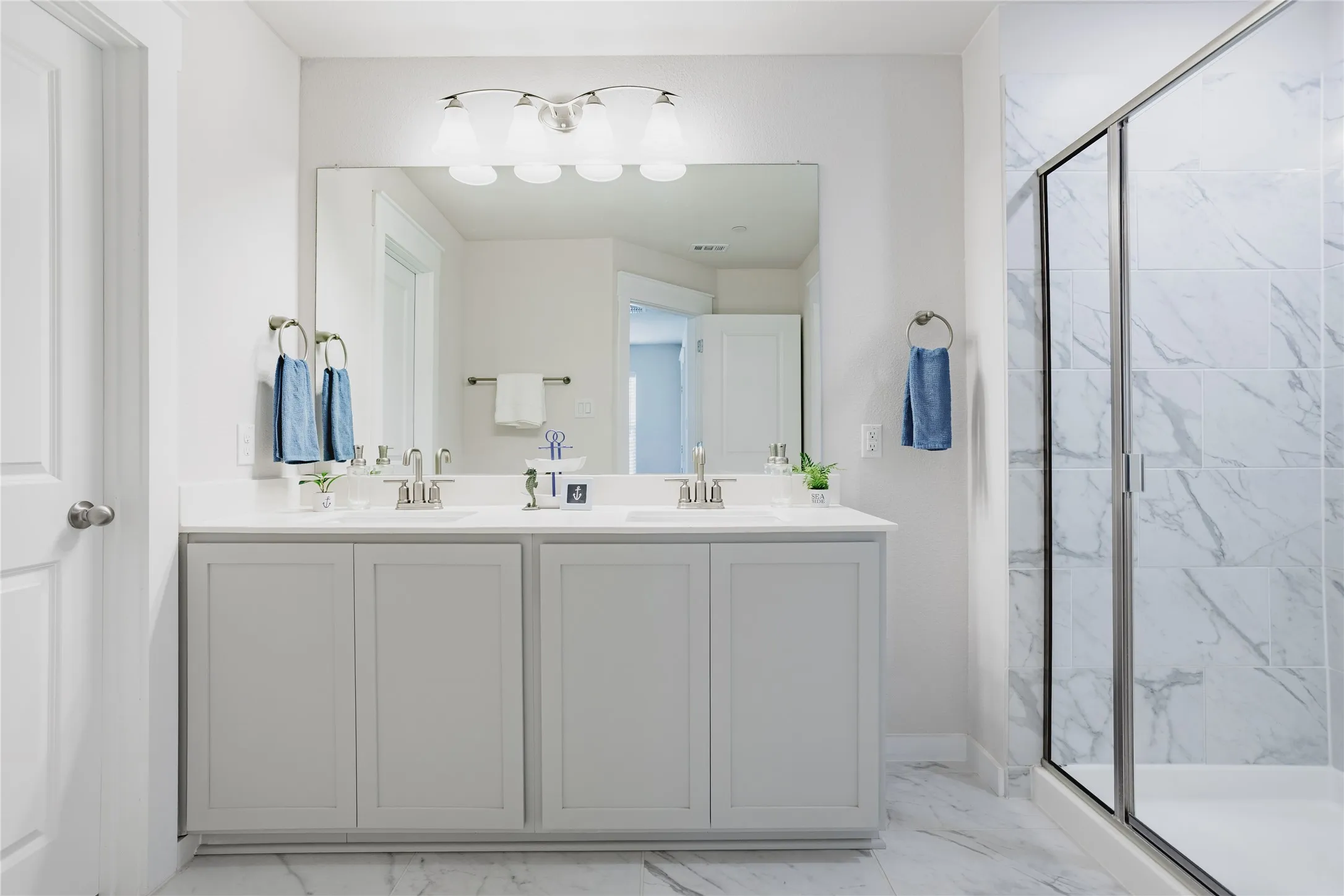 Double vanity with brushed nickel fixtures, light-toned cabinetry, large mirror, and a glass-enclosed shower featuring tile surround