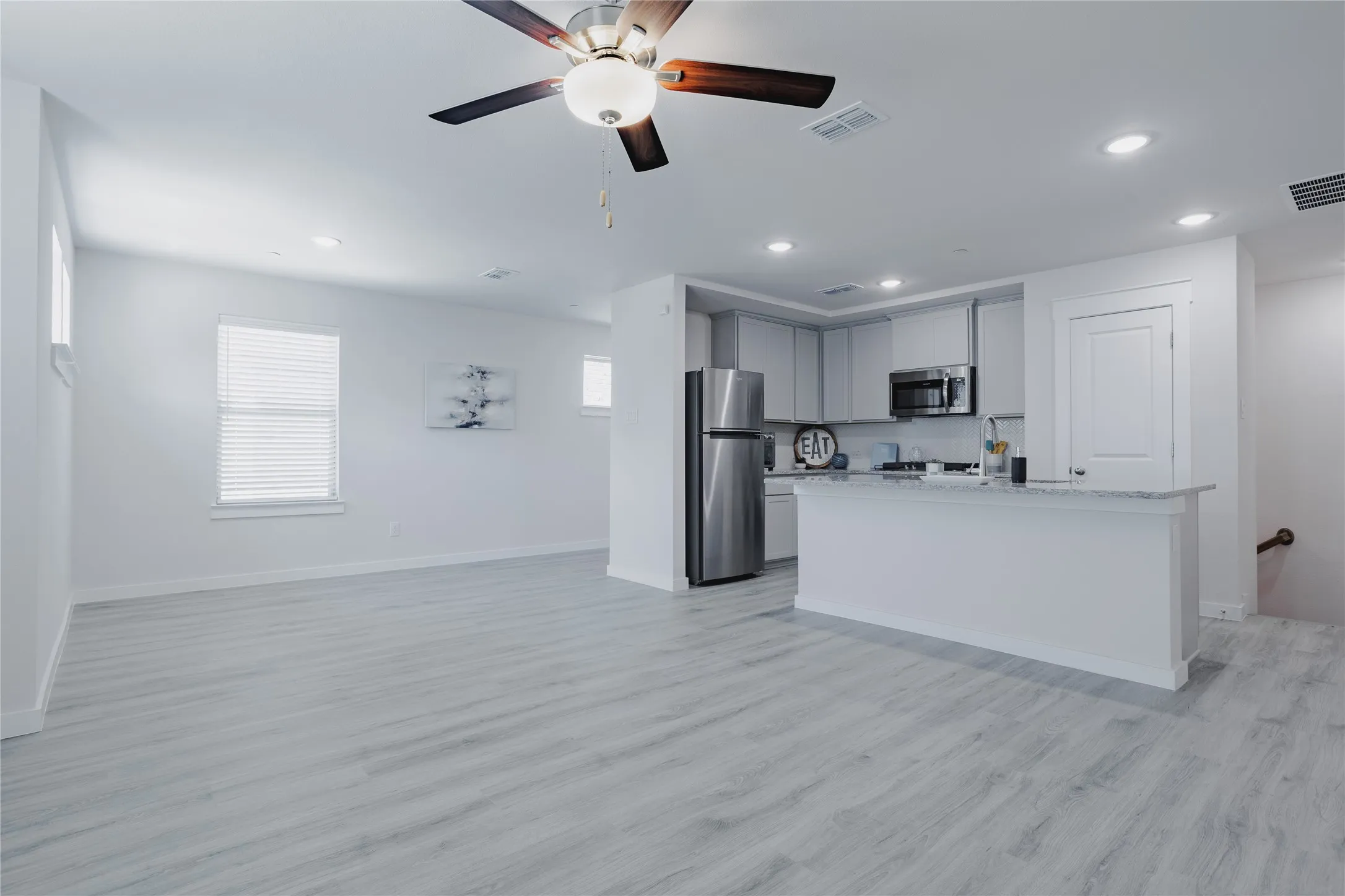 Open-concept living area featuring wood-finish flooring, a ceiling fan with integrated lighting, and recessed lighting