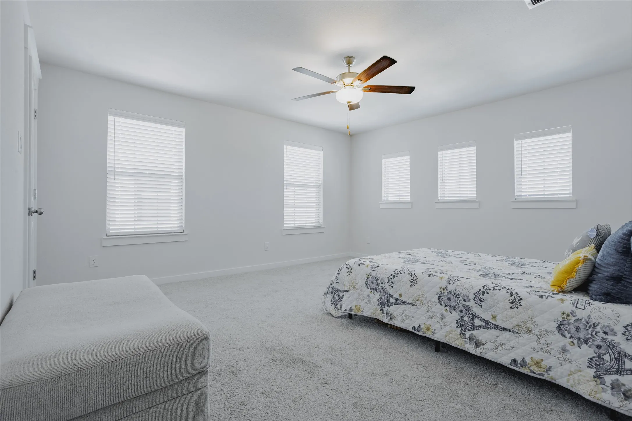 Spacious room featuring light gray carpeting, multiple windows with white blinds, a ceiling fan with integrated lighting, and white painted walls