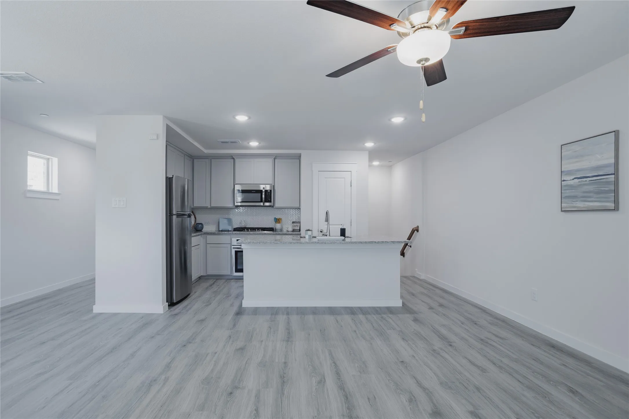 Open-concept kitchen featuring an island with a light-toned countertop, stainless steel appliances, light gray cabinetry, and recessed lighting