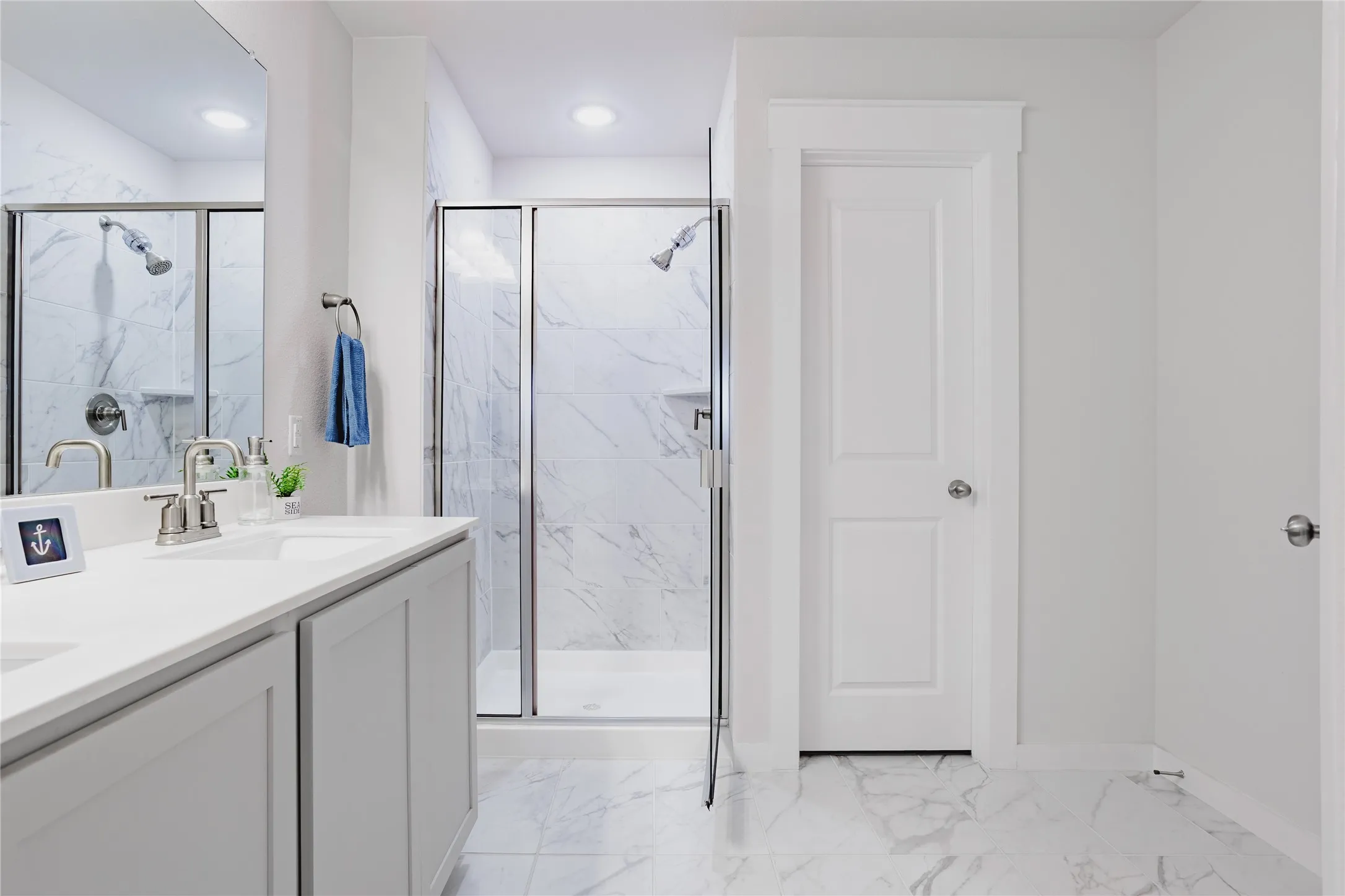 Spacious bathroom featuring a double vanity with stone countertops, a walk-in shower with clear glass enclosure, and large format tile flooring