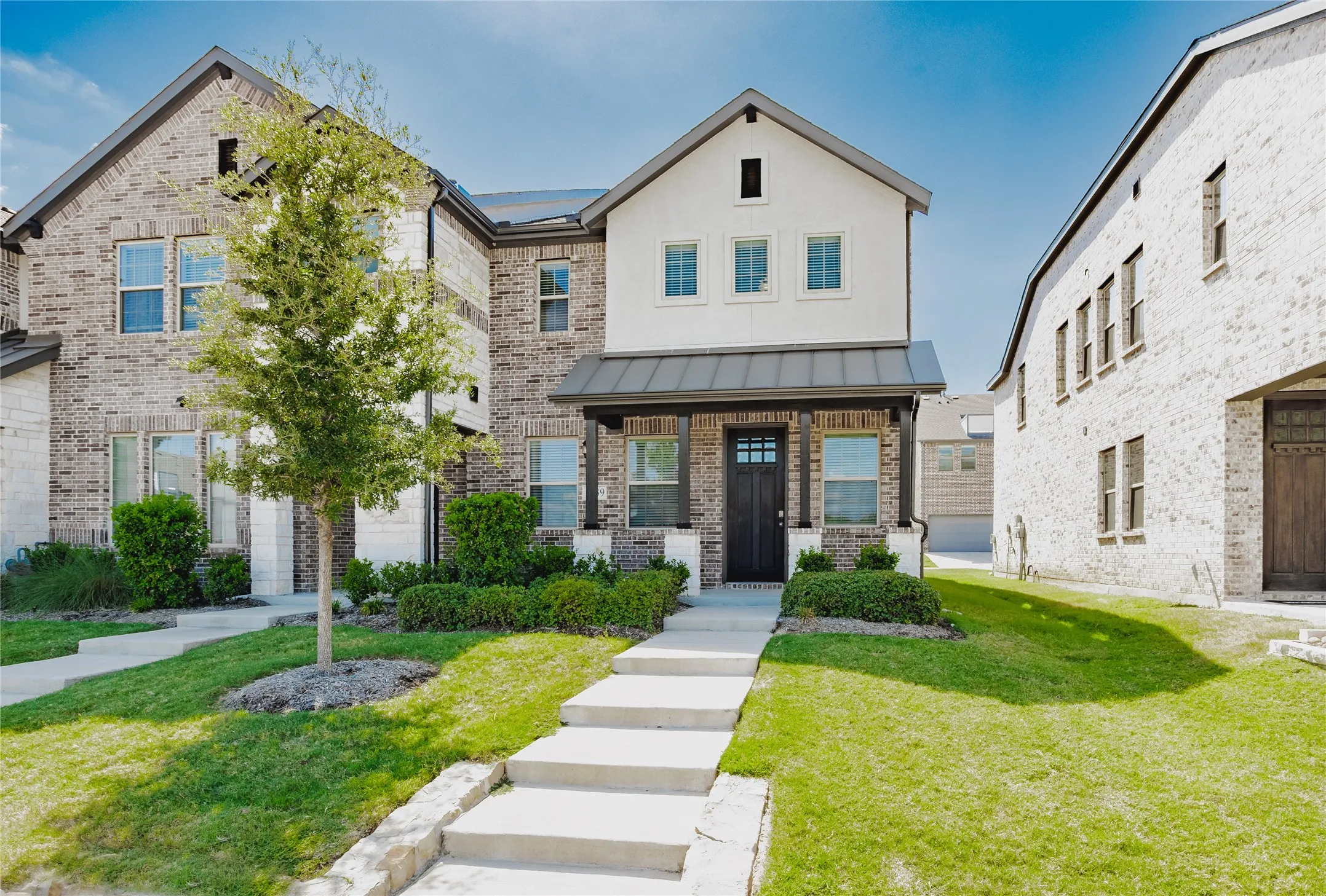 Brick and stucco exterior with multiple gables, covered porch with columns, dark paneled front door, and a concrete walkway