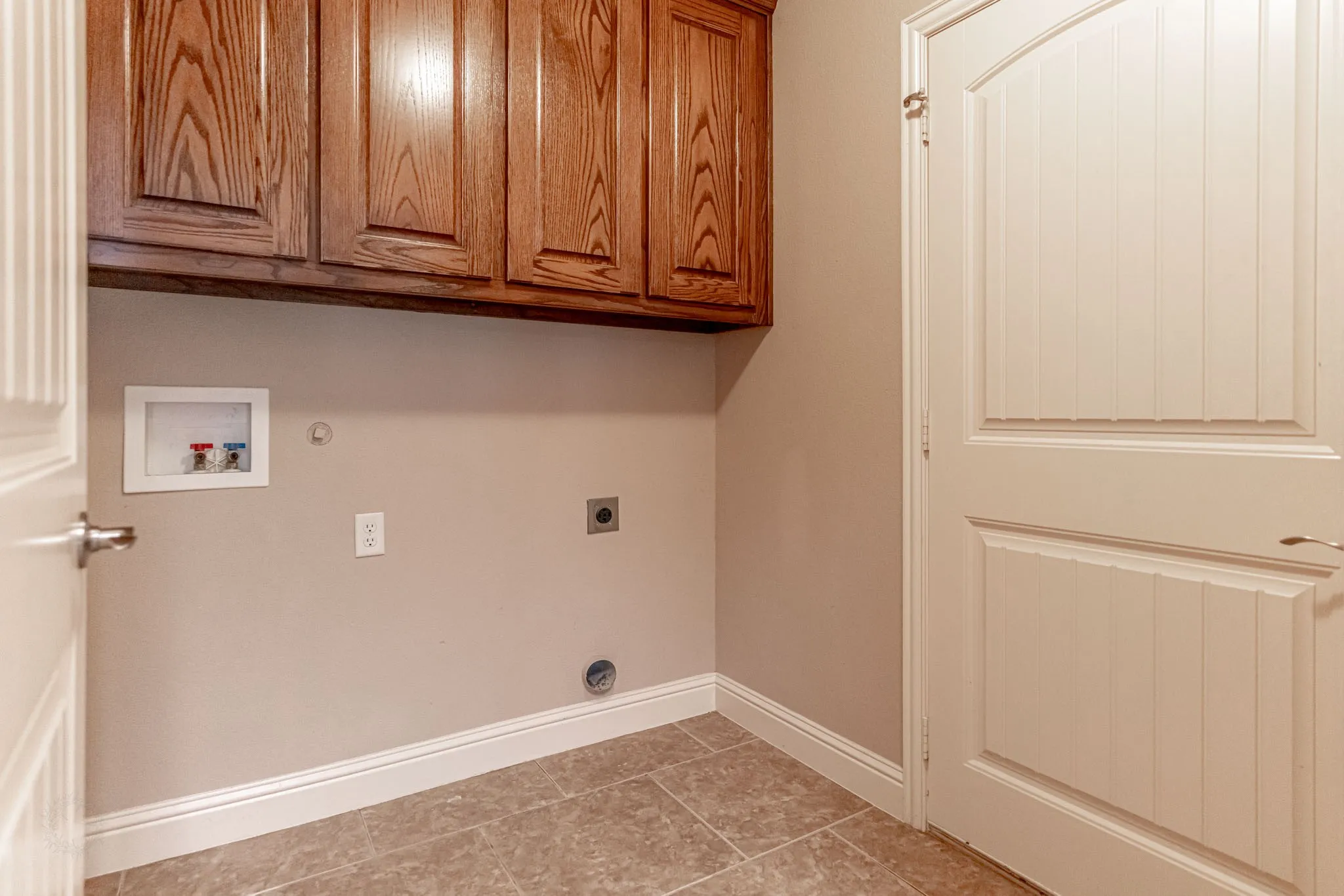 Large utility room with washer/dryer hook ups and over hanging cabinets for storage