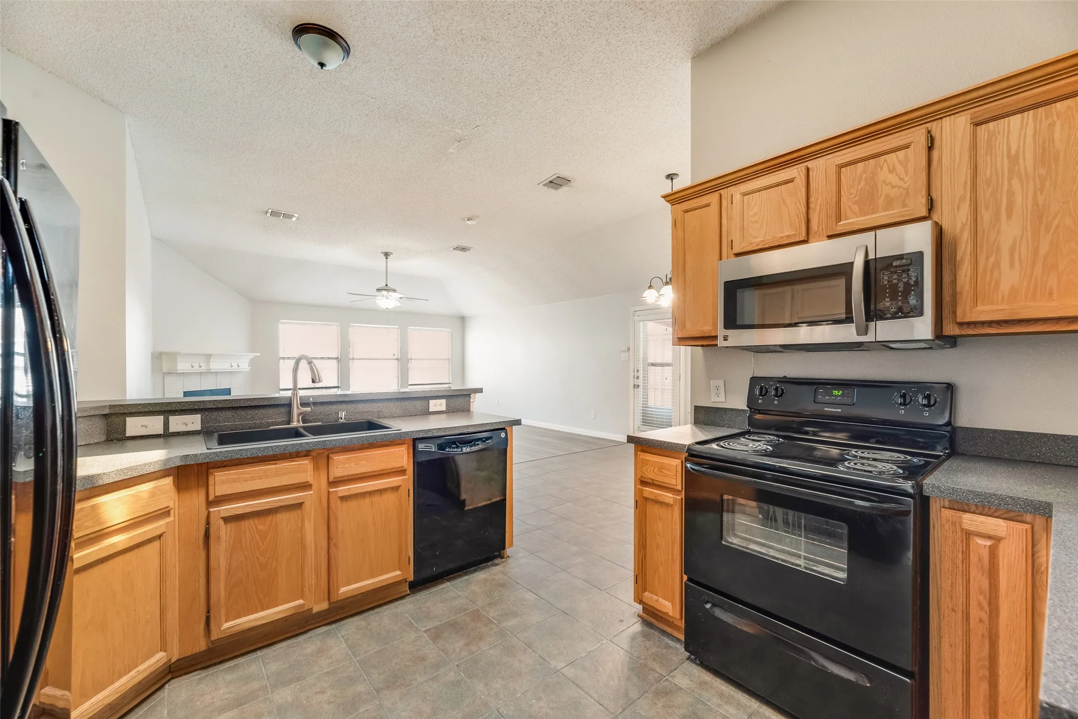 Kitchen featuring wood cabinetry, dark countertops, a stainless steel microwave, black electric range, and a built-in dishwasher