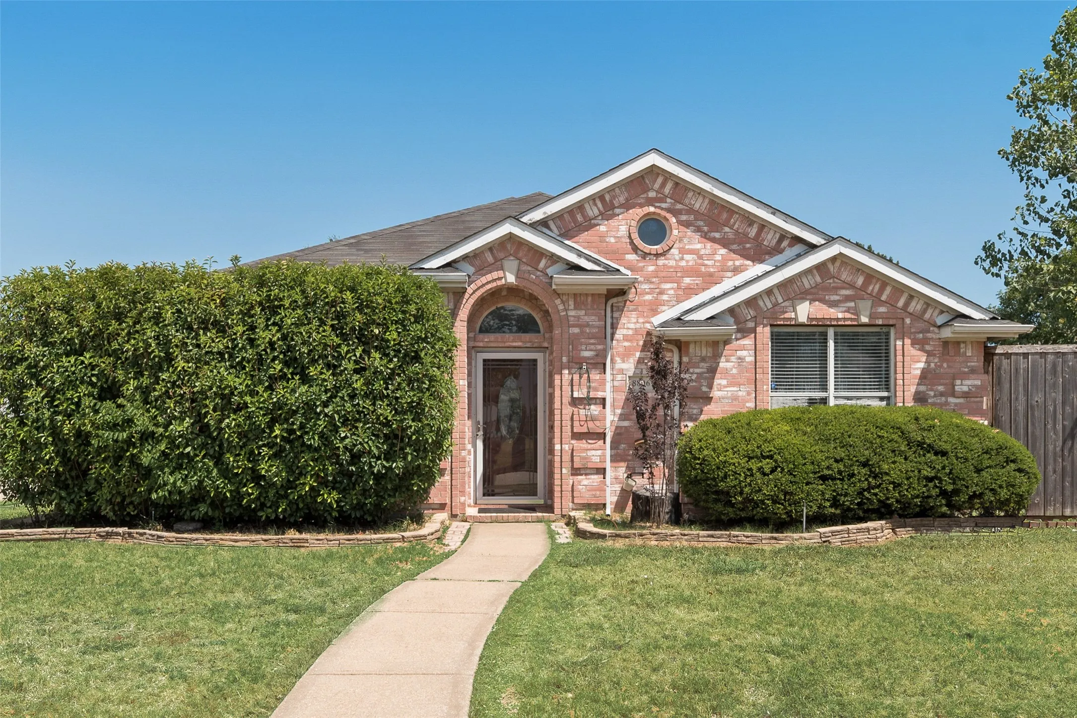 Brick exterior with an arched entryway, established landscaping, and a concrete pathway