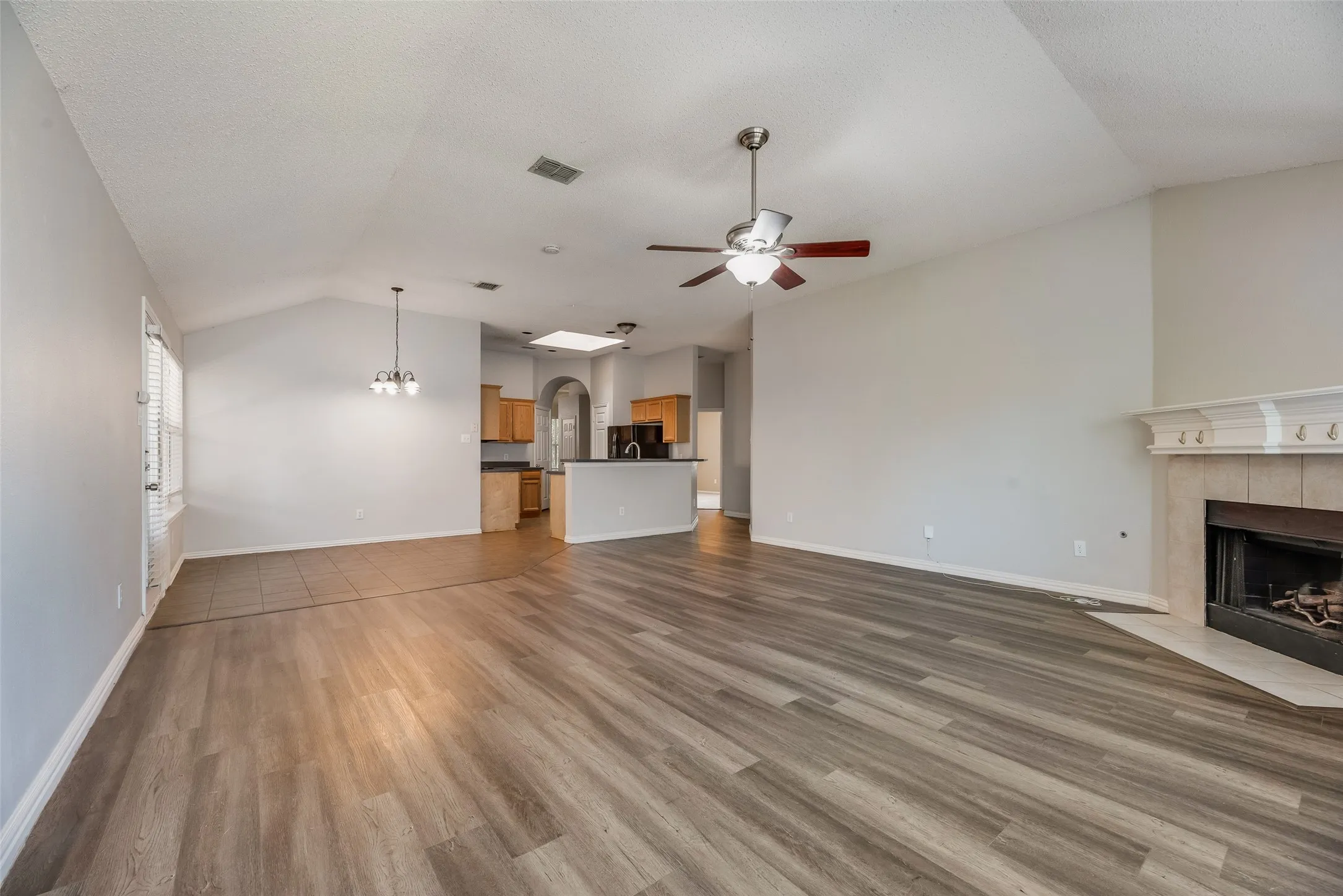 Vaulted ceiling with ceiling fan, wood-finish flooring, tile-surround fireplace with mantel, and built-in archway