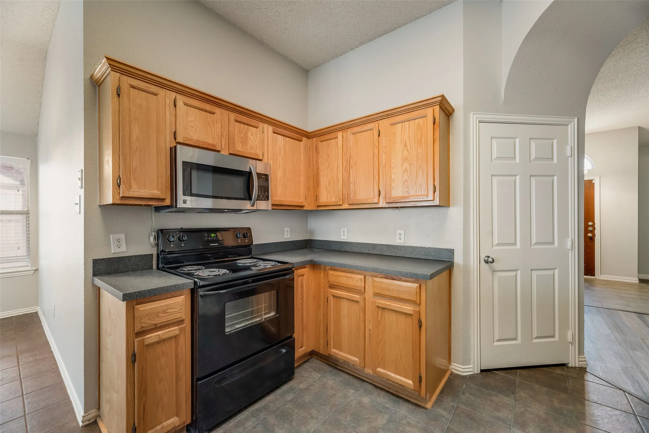 Kitchen featuring wood-finish cabinetry, dark countertops, a black electric range, and a stainless steel microwave