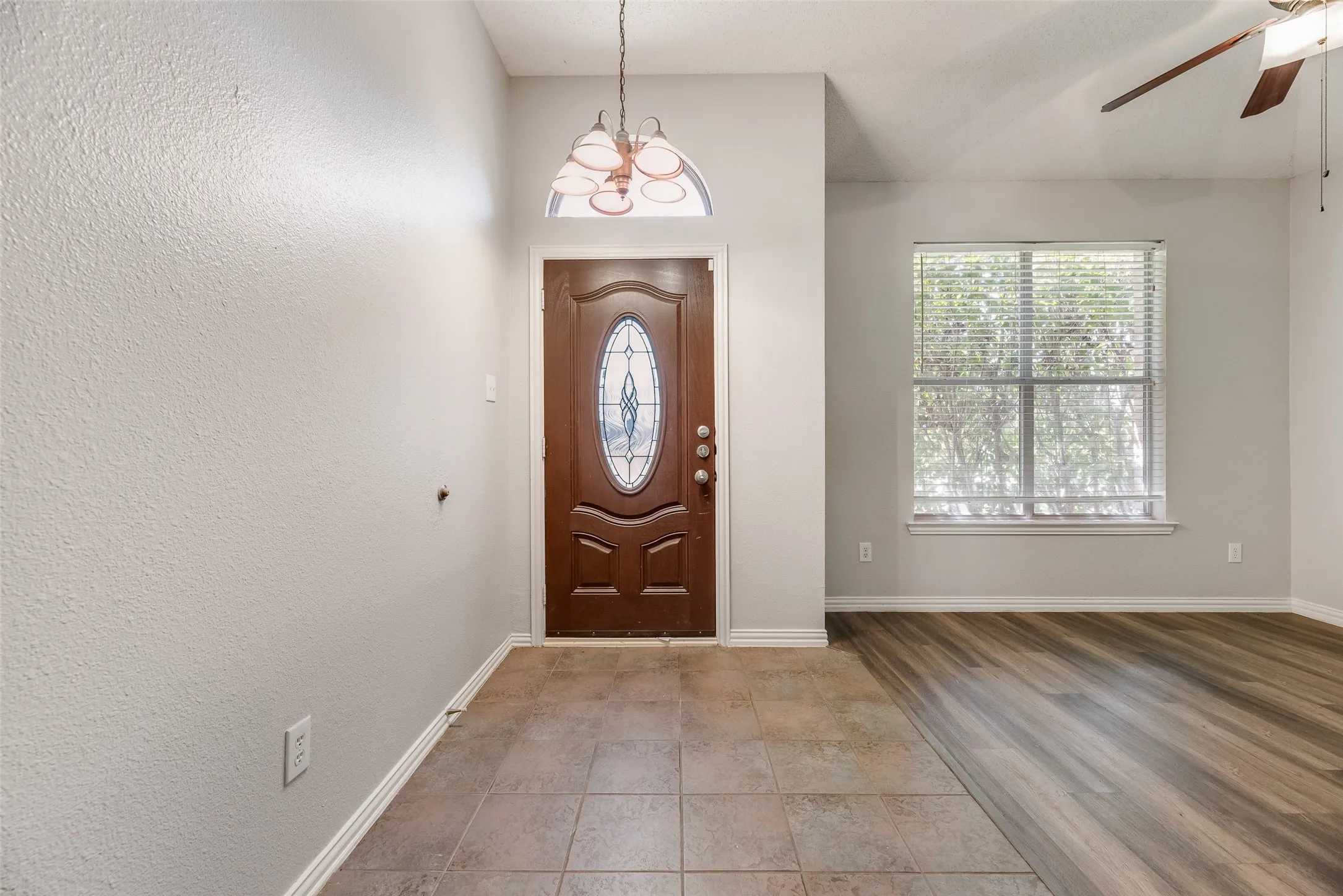 Entryway featuring a decorative wood-panel door with oval glass insert, transom window, and tile flooring