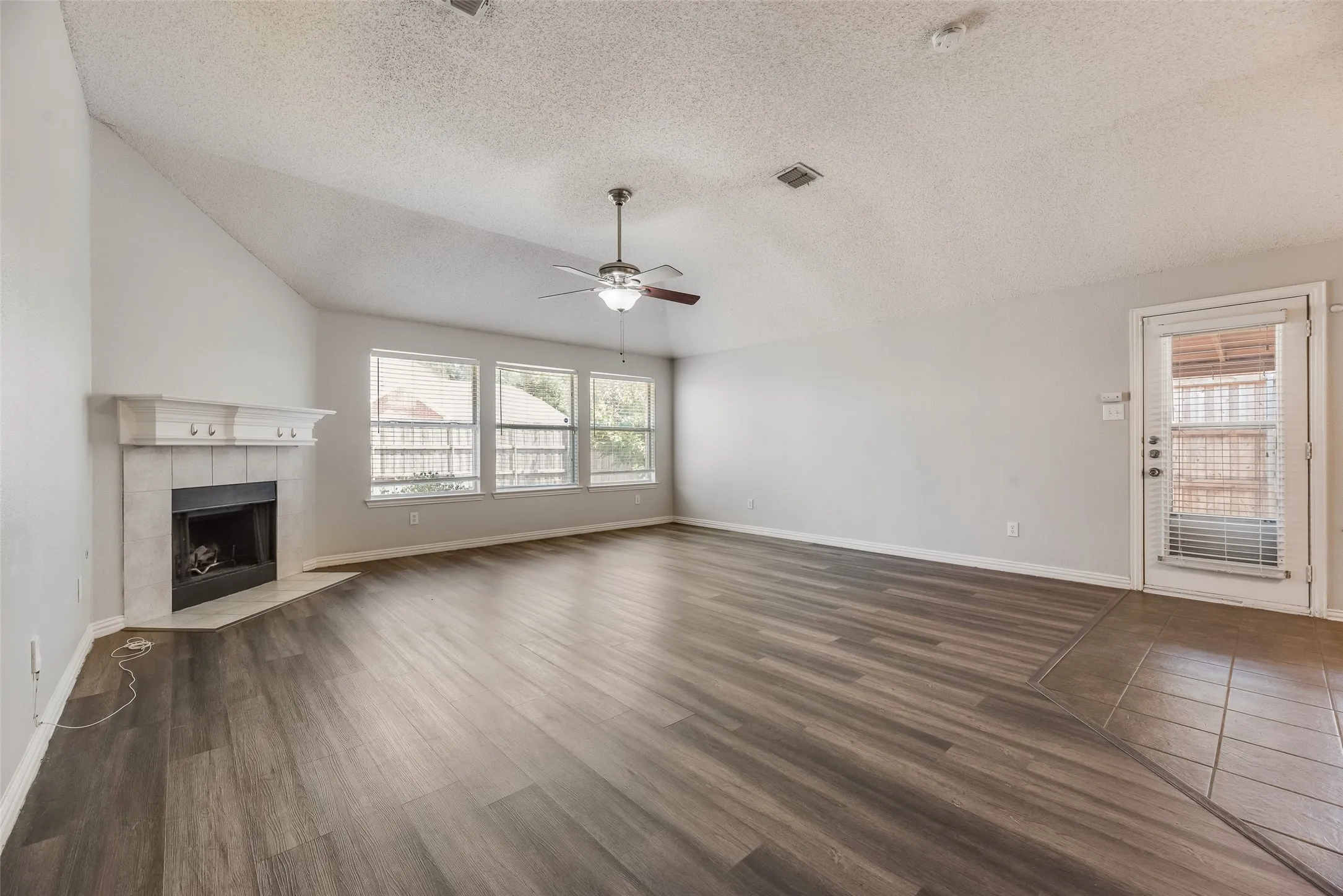Angled fireplace with a substantial mantelpiece, vaulted ceiling, wood-finish flooring, and multiple windows