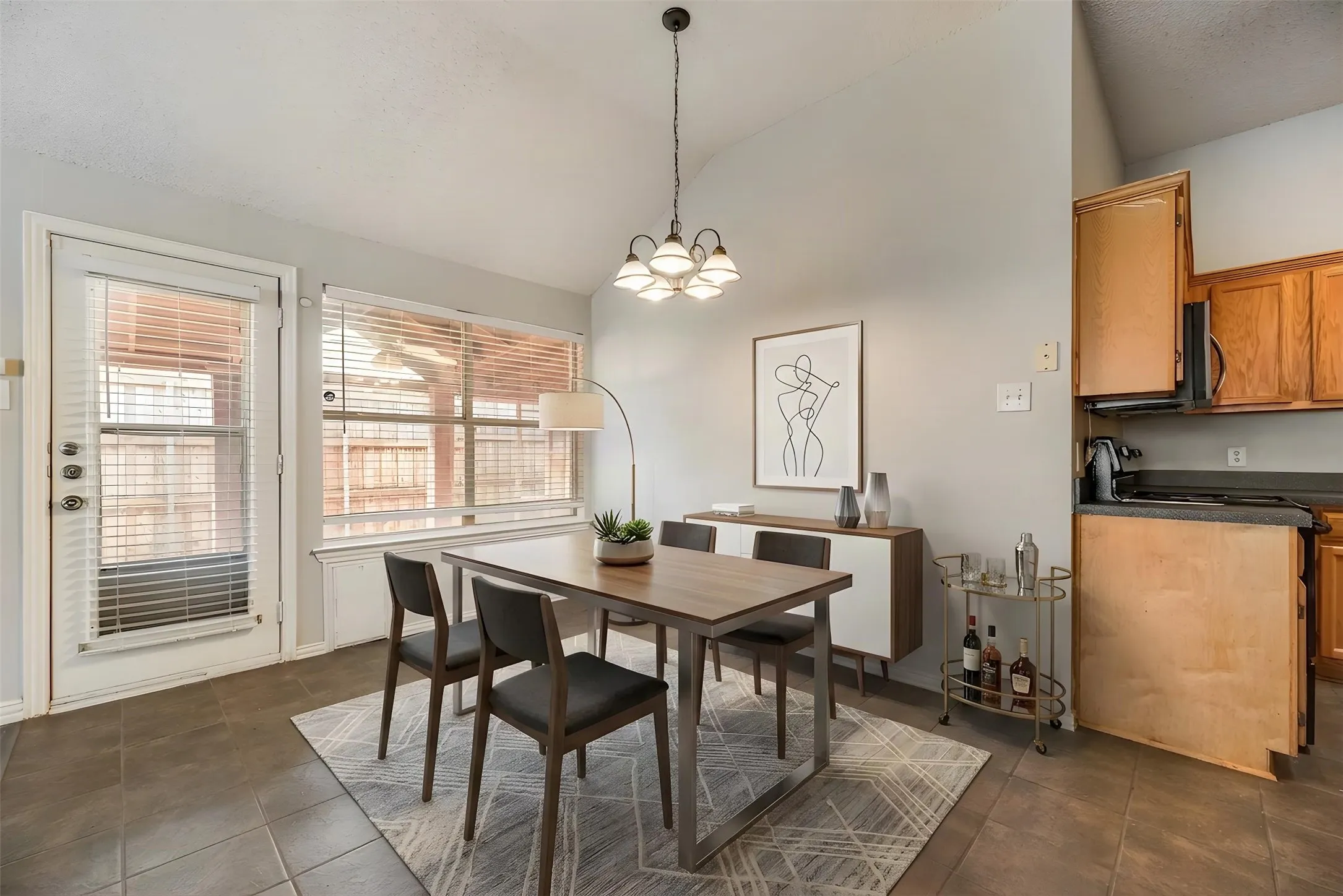 Open-concept dining and kitchen area featuring a wood-finish dining table, pendant lighting fixture, tile flooring, wood-finish cabinetry, and stainless steel appliances