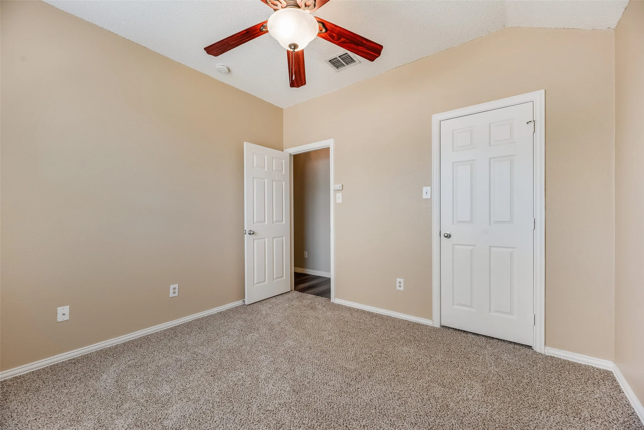 Neutral wall paint, textured carpeting, sloped ceiling, ceiling fan with light fixture, and white paneled doors