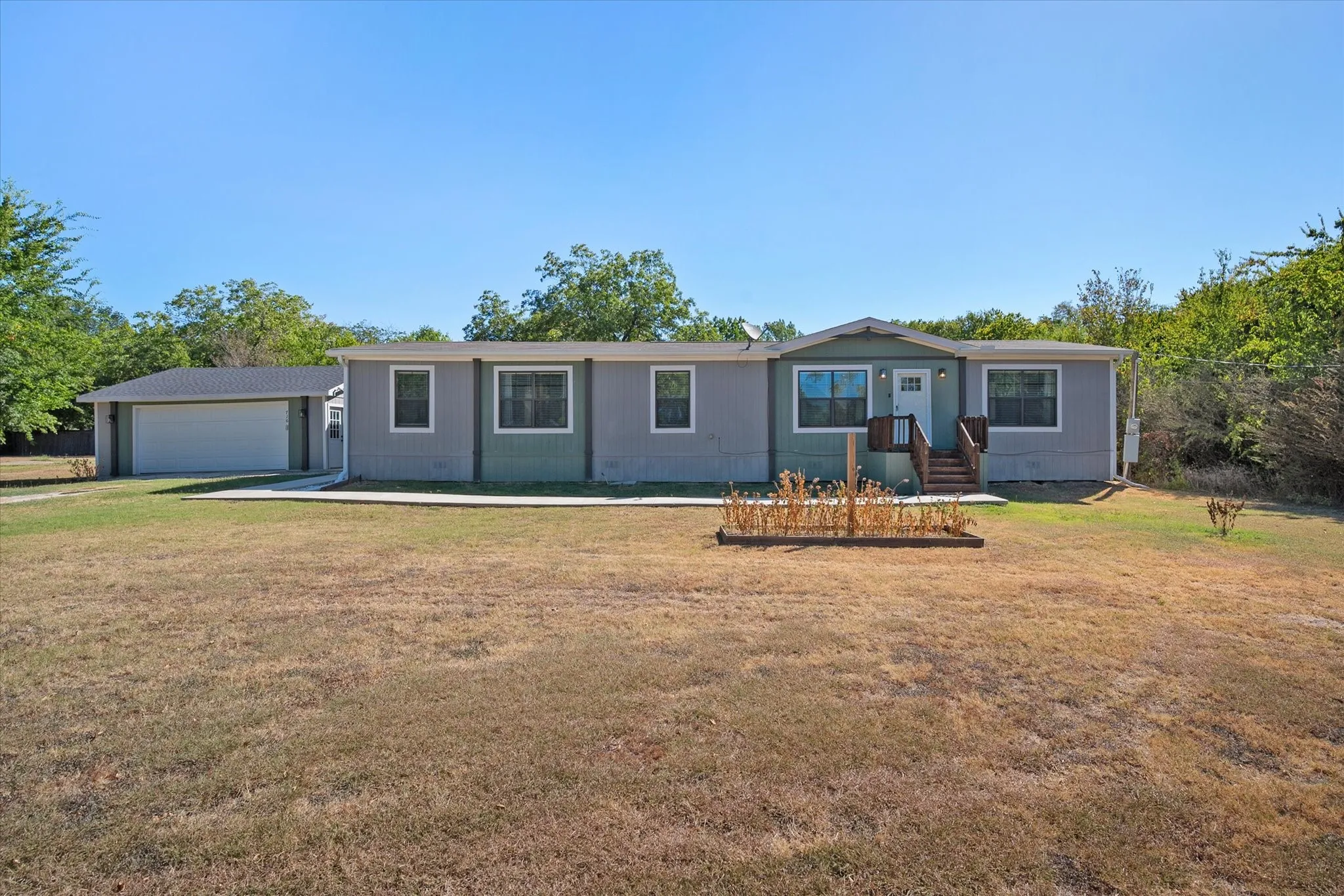 Front exterior view showcases the long single-story home, detached garage, spacious lawn and convenient walkway to the entrance.