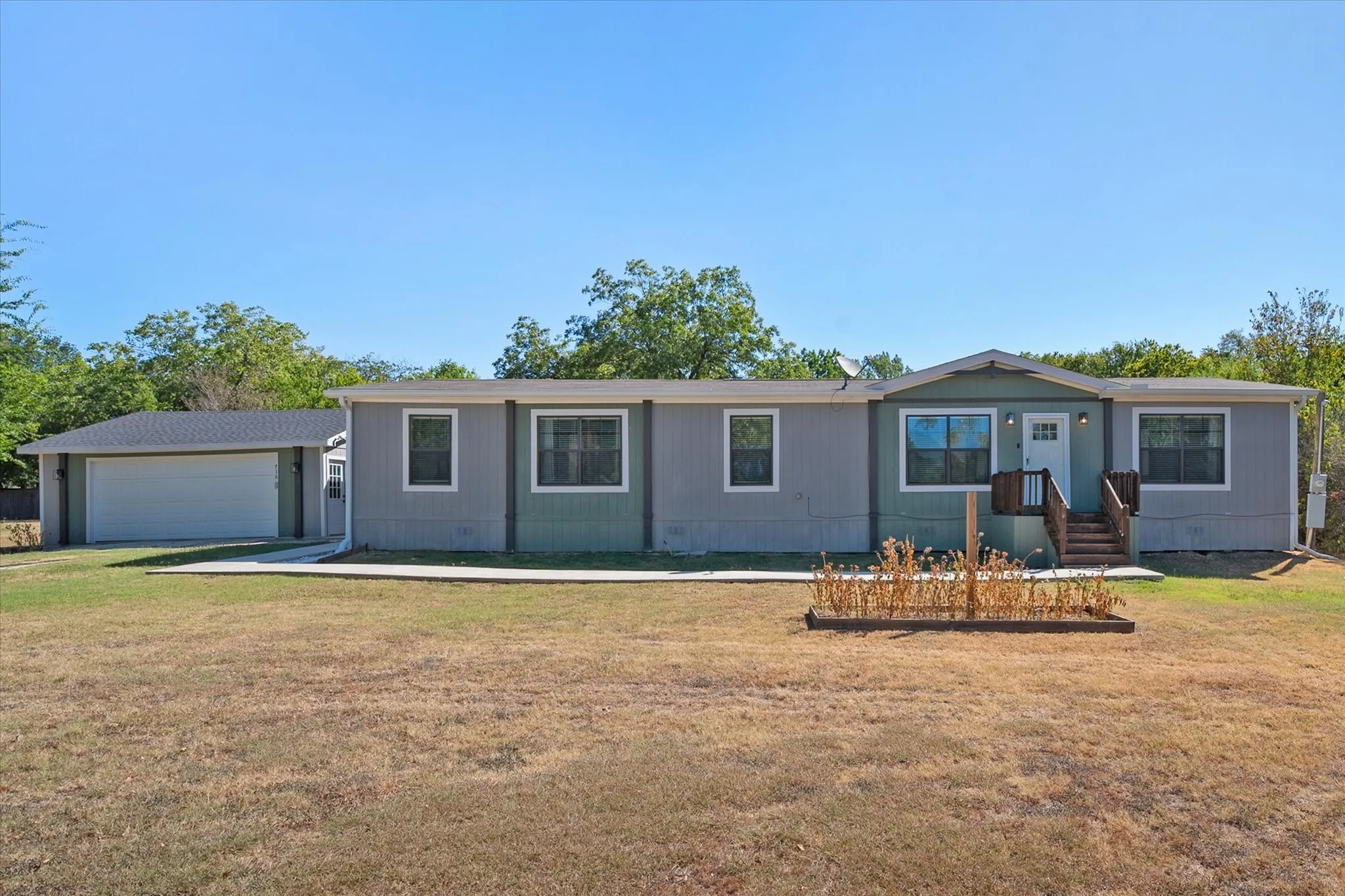 Wide front view of this 2022 Kerens TX home highlights the detached garage, expansive yard and inviting single-story design.
