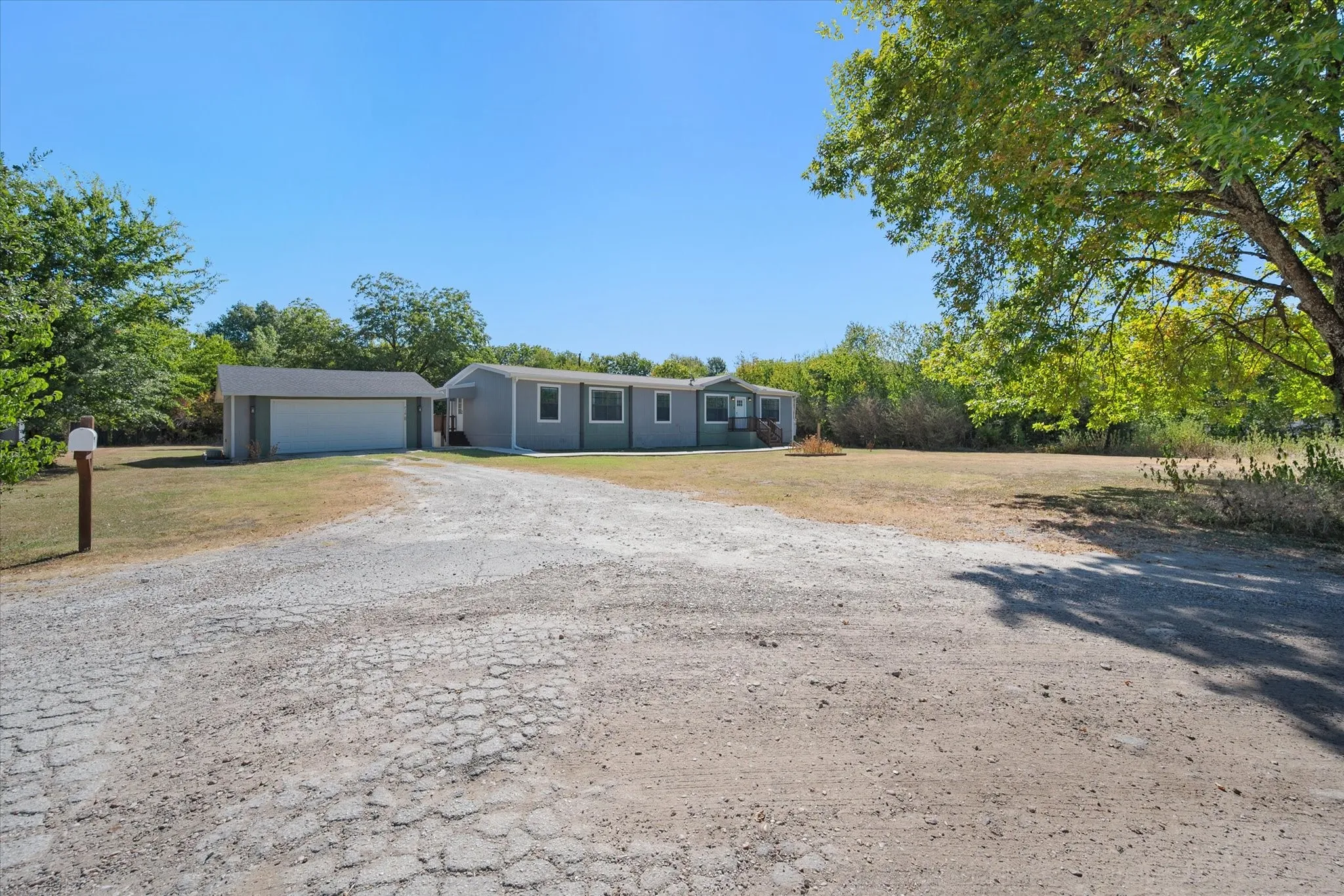 Wide front property view highlights the detached garage, extended driveway area, mature trees and spacious setting at this Kerens TX home.