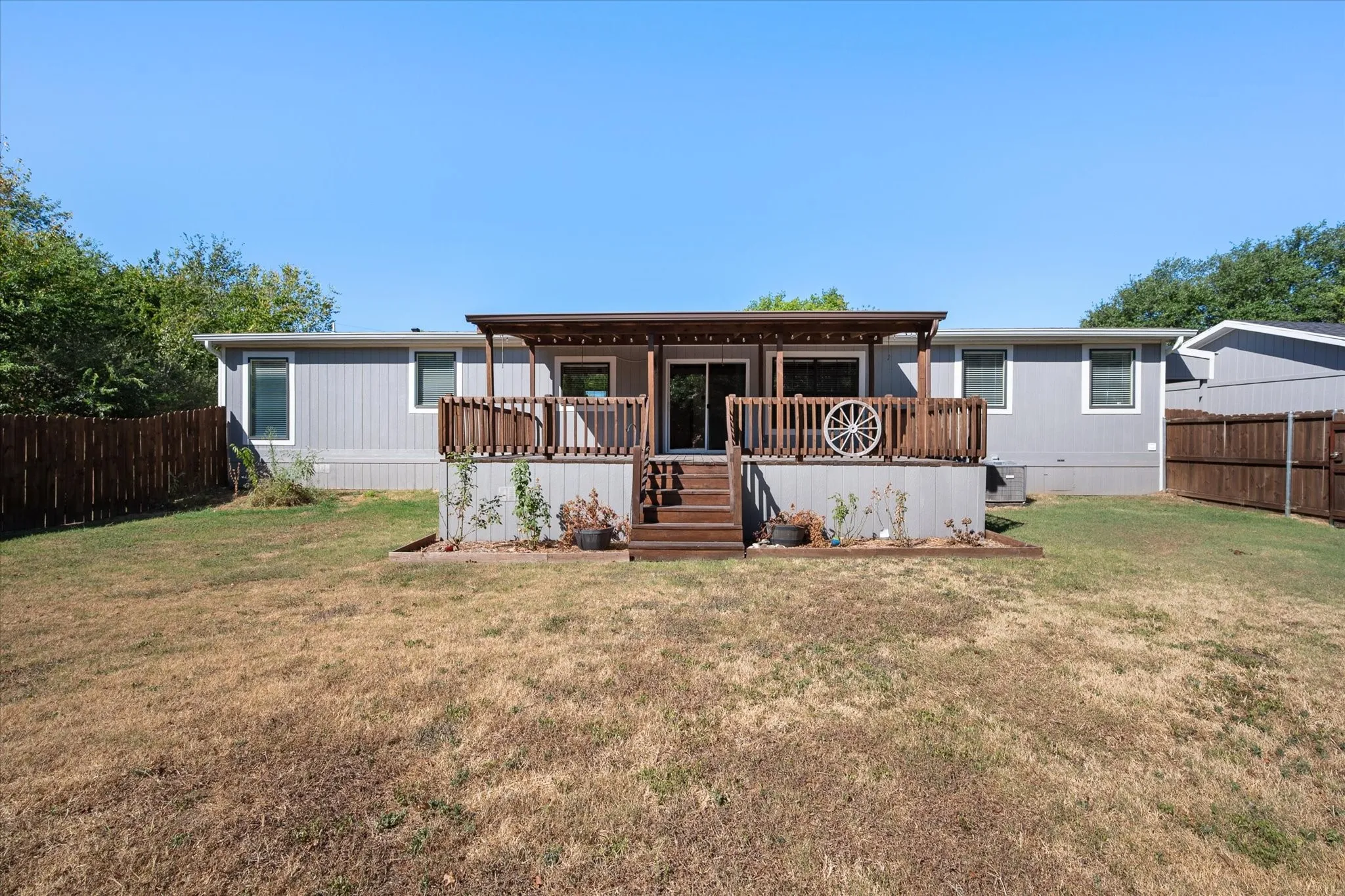 Rear exterior view showcases the home's covered deck, fenced backyard and generous outdoor space on the 0.568-acre property.