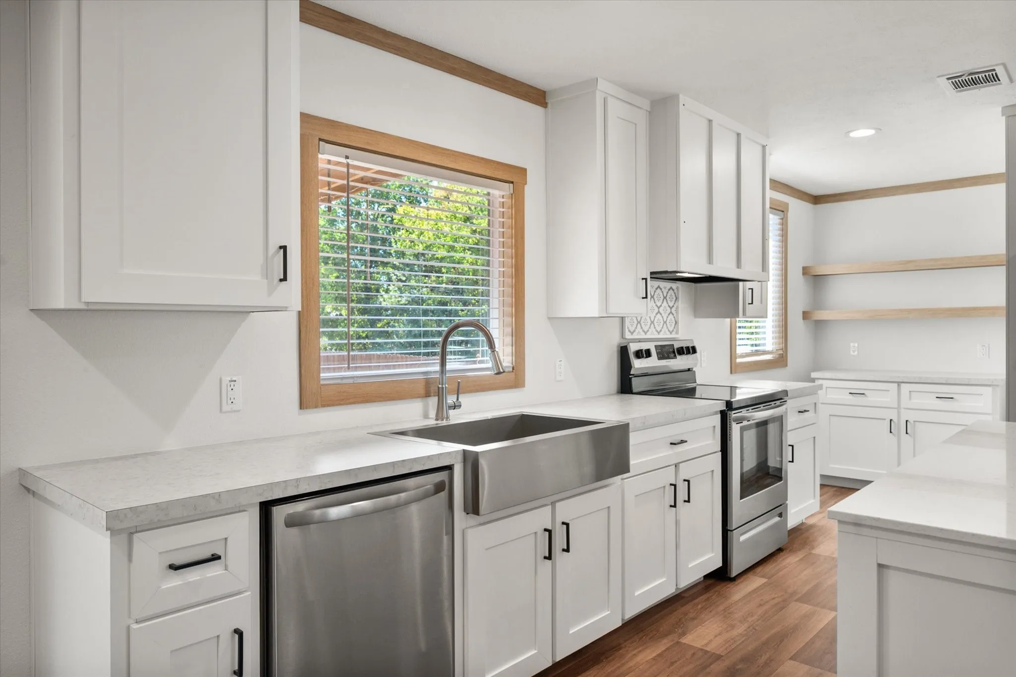 Bright kitchen workspace with granite-style counters, stainless steel dishwasher, generous cabinetry and window overlooking the property