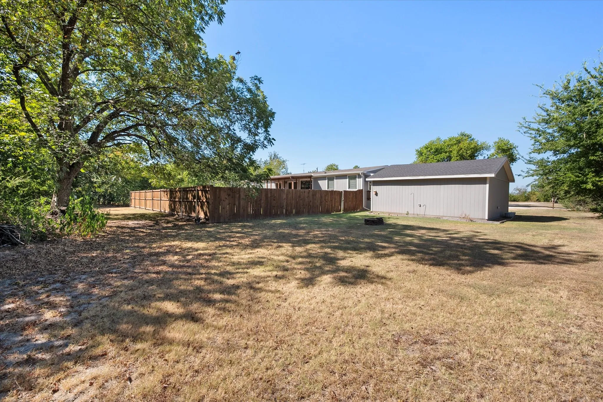 Side and rear property view highlights the generous lot, mature shade trees, fenced backyard and detached garage.