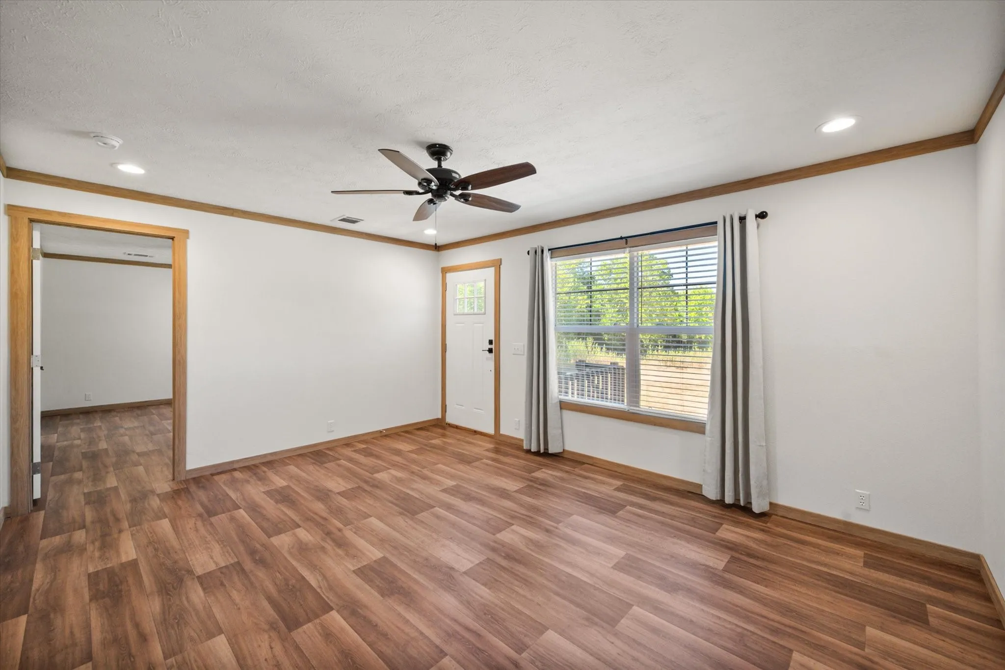Generously sized living room features wood-look flooring, ceiling fan, recessed lighting and natural light from the front-facing window, and leads to the primary suite.