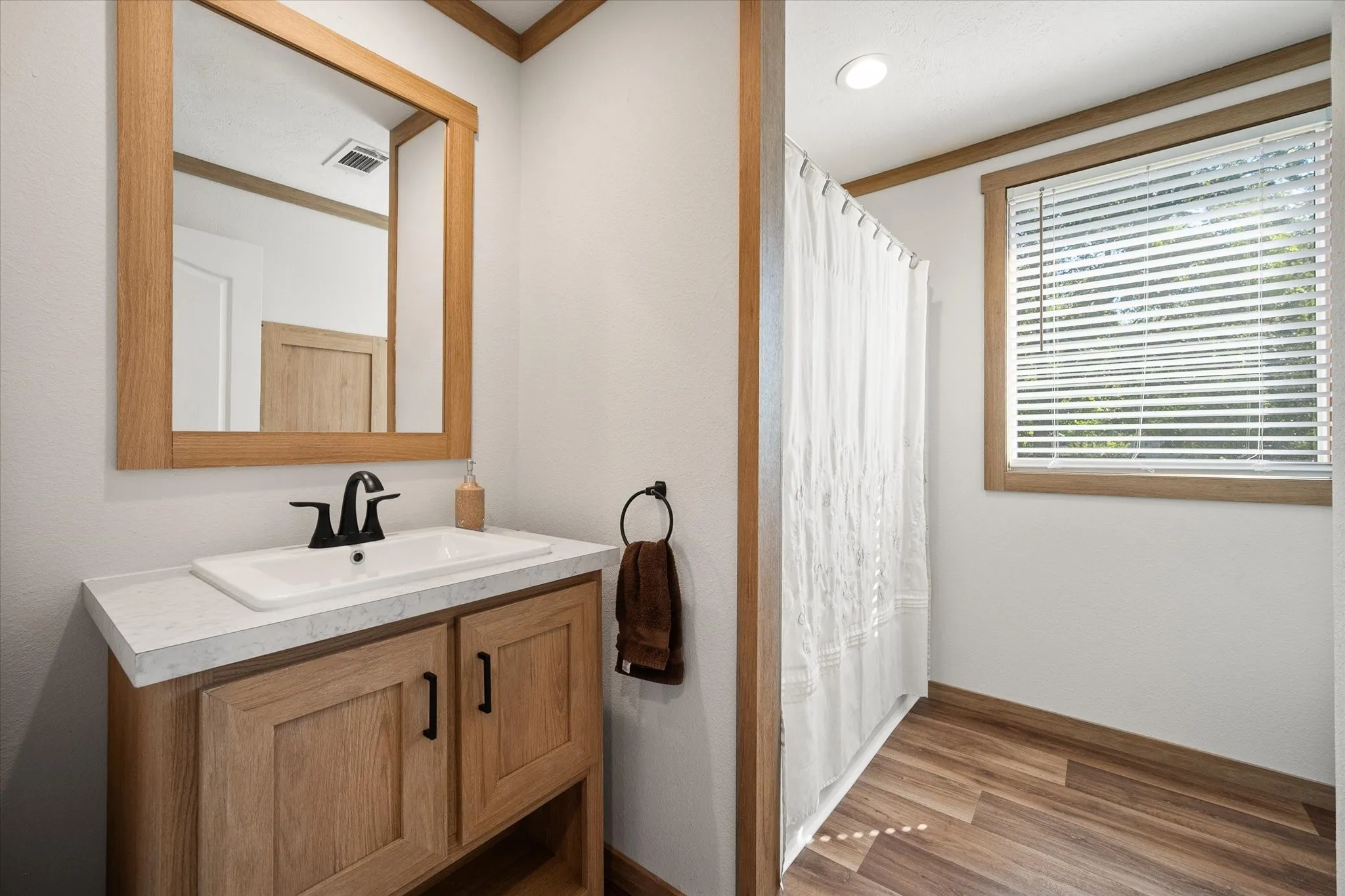 Full guest bathroom features a modern vanity, shower-tub combination, window and attractive wood-look flooring.
