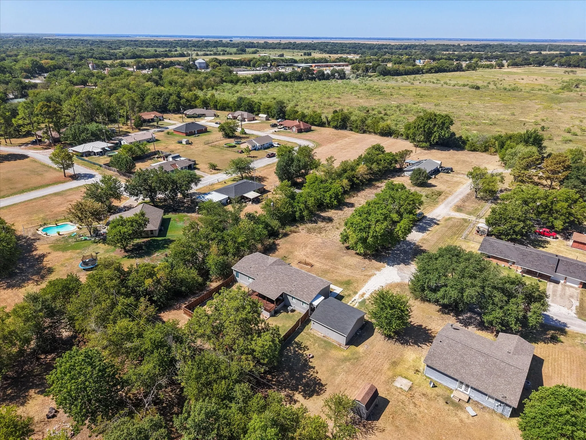 Aerial view showcases the property's neighborhood setting with mature trees, nearby homes and expansive open land beyond Kerens.