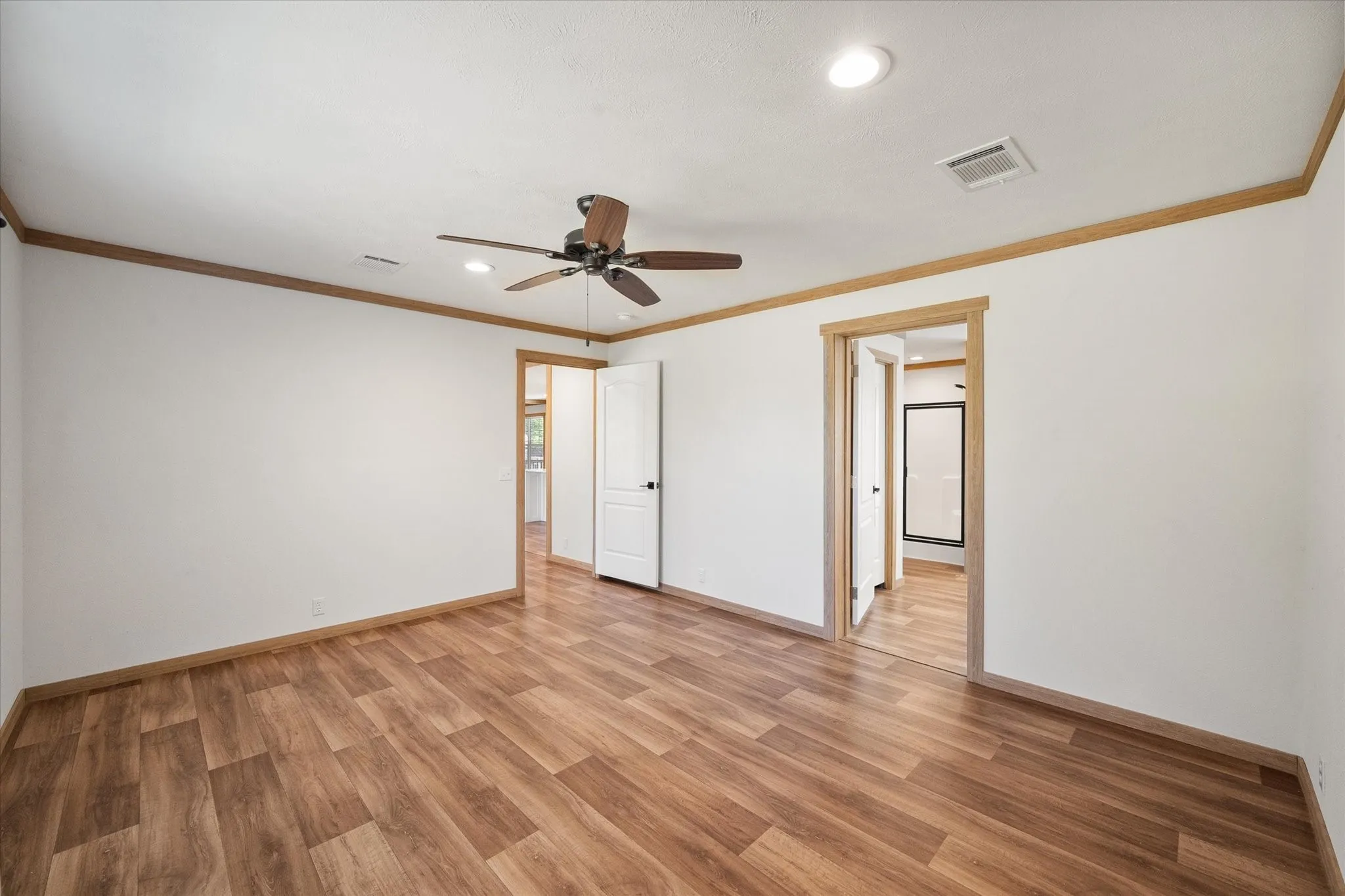 Spacious primary bedroom features wood-look flooring, ceiling fan, recessed lighting and convenient access to the ensuite bathroom.