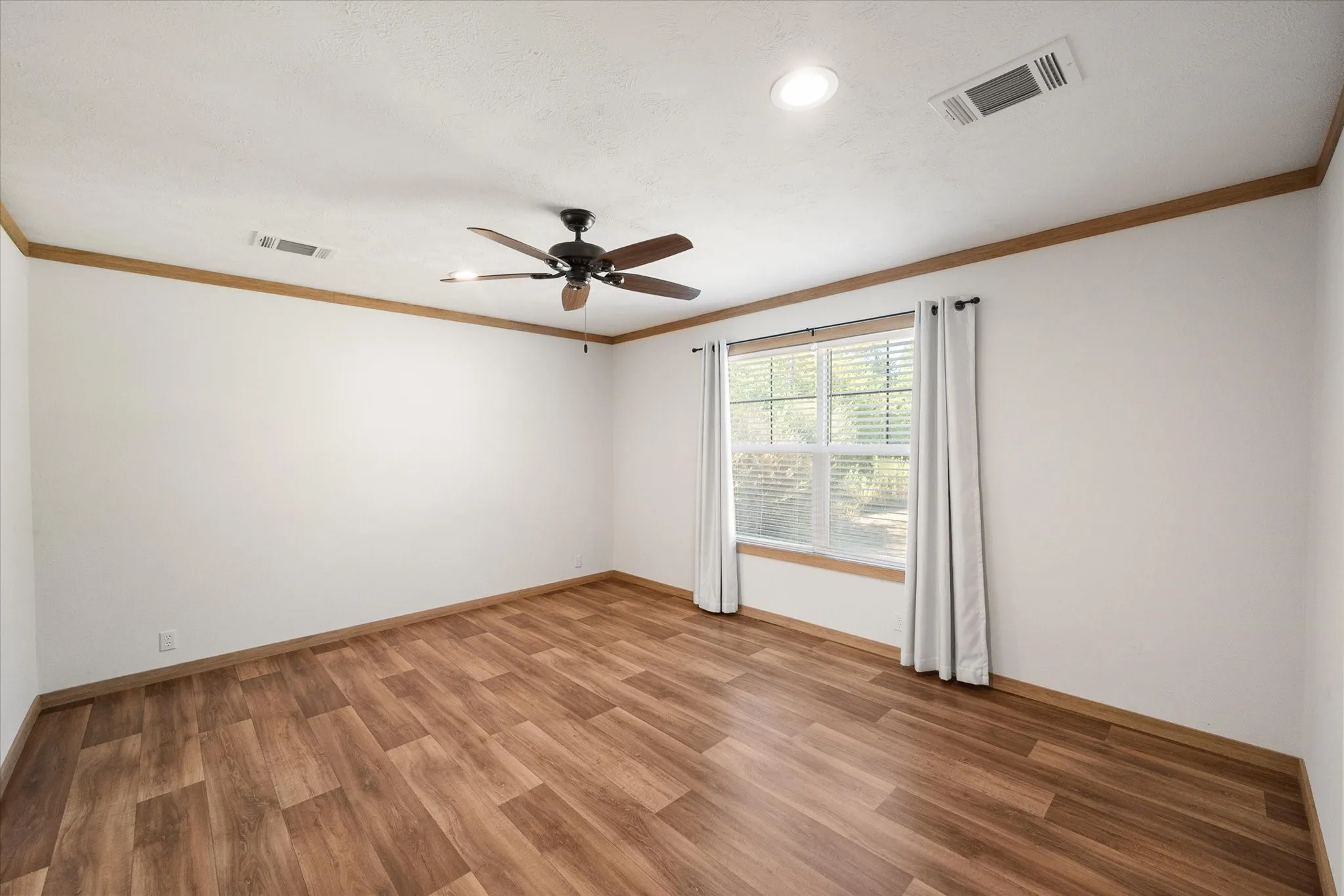 Comfortable primary bedroom offers a ceiling fan, large window and easy-care wood-look flooring.