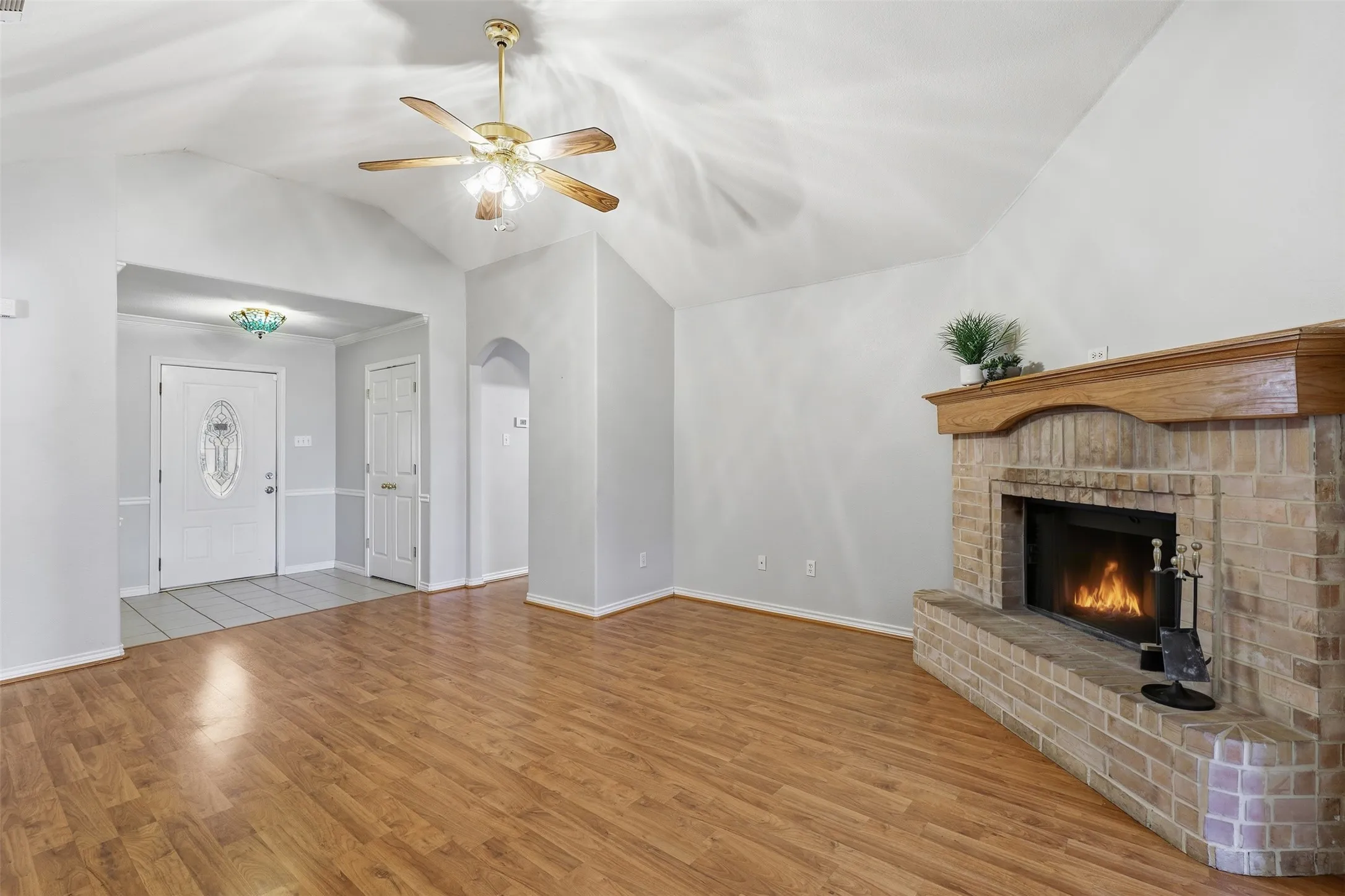 Wood-finish flooring, vaulted ceiling with a ceiling fan, and a brick fireplace with a wood mantel
