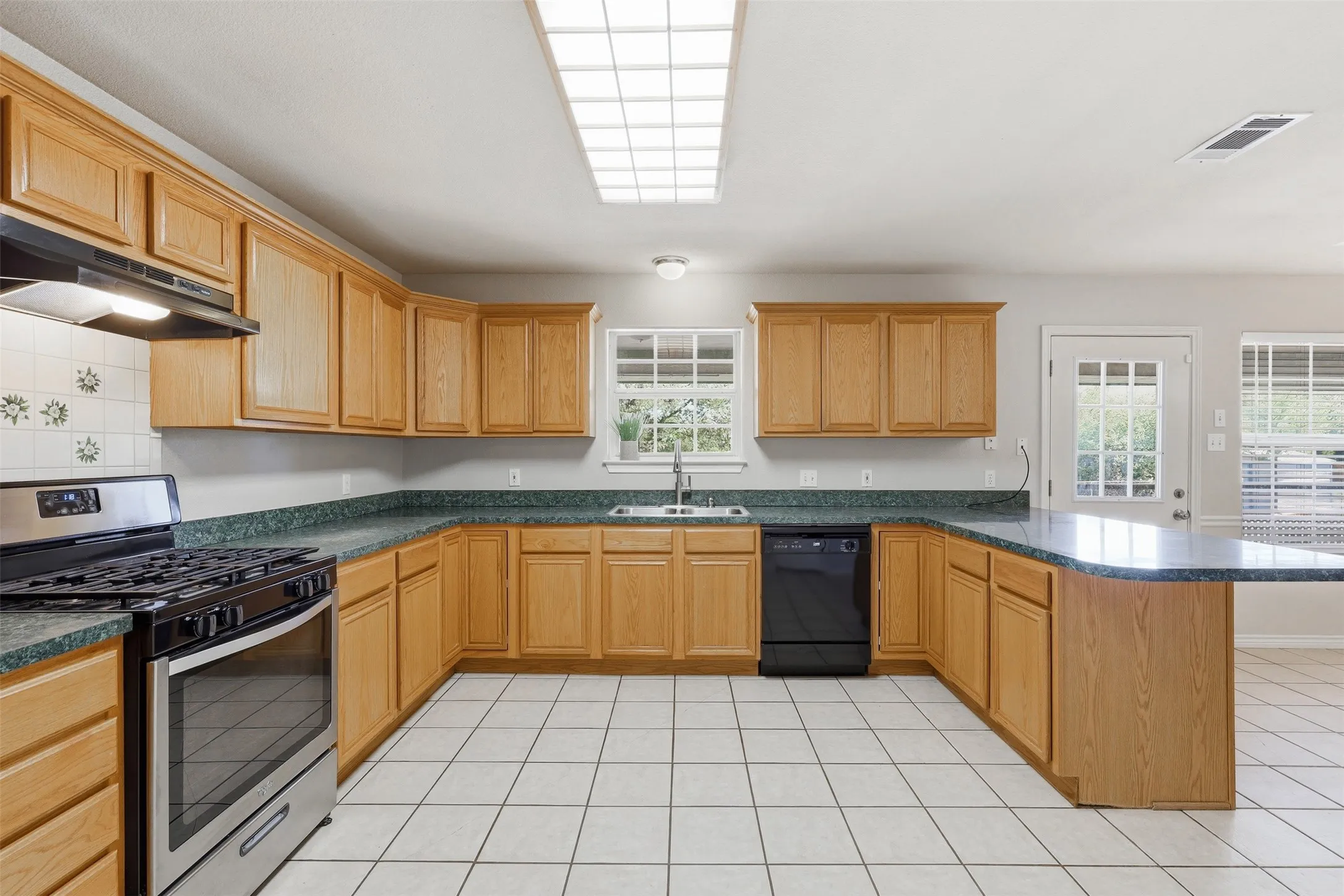 U-shaped kitchen layout featuring wood cabinetry, integrated stainless steel range, and tile flooring