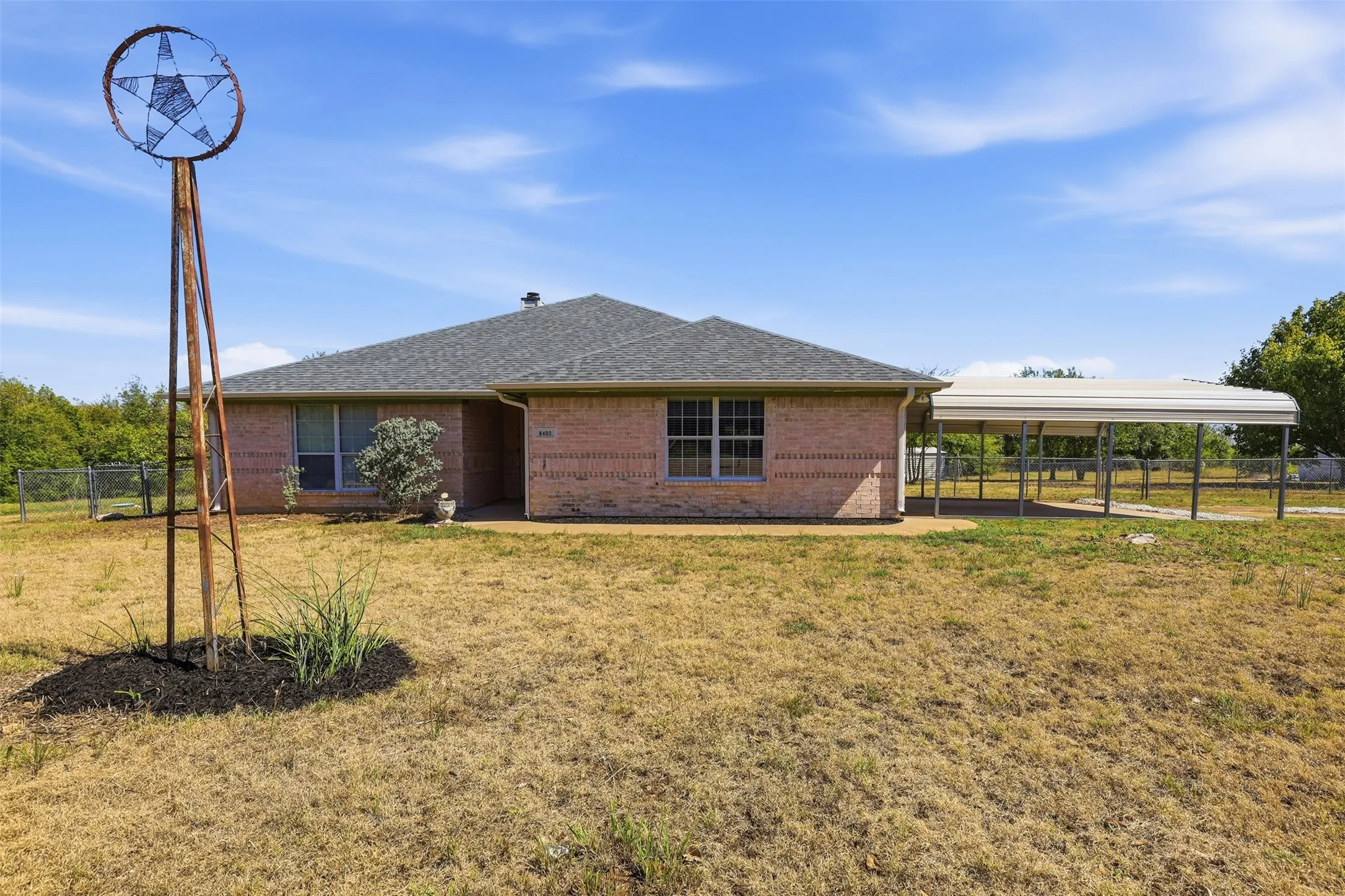 Brick exterior, pitched shingle roof, attached carport, fenced perimeter, decorative metal windmill