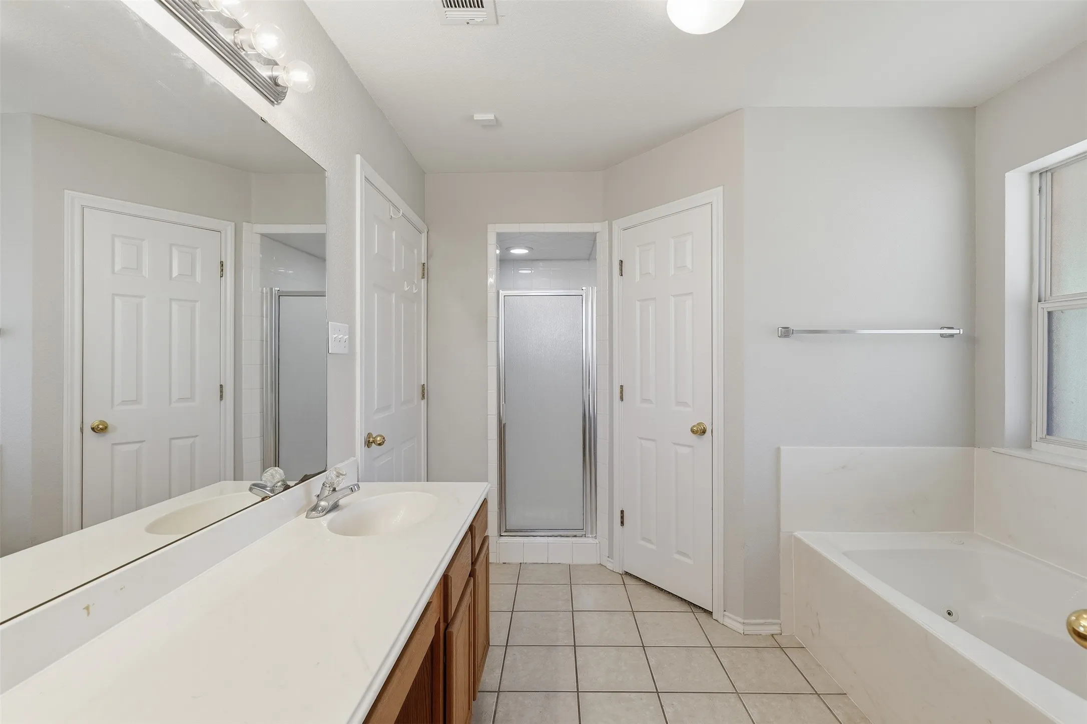 Double vanity with integrated sinks, wood-finish cabinetry, frameless mirror, and a built-in tub