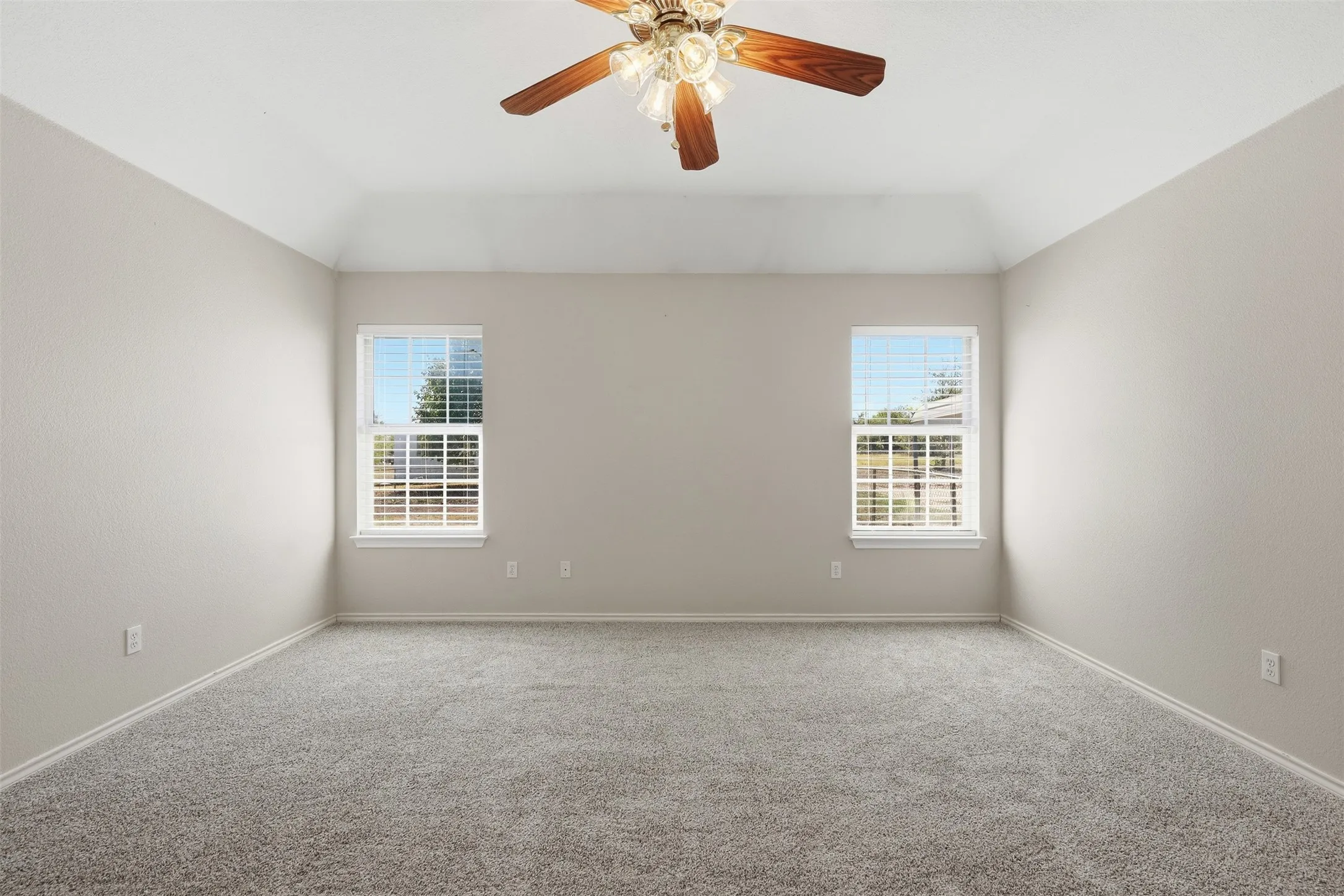 Neutral-toned carpeting, vaulted ceiling with a ceiling fan, and two windows with blinds