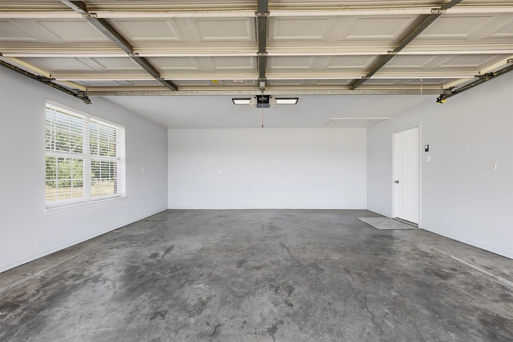 Spacious garage featuring a concrete floor, two windows with blinds, and white interior door