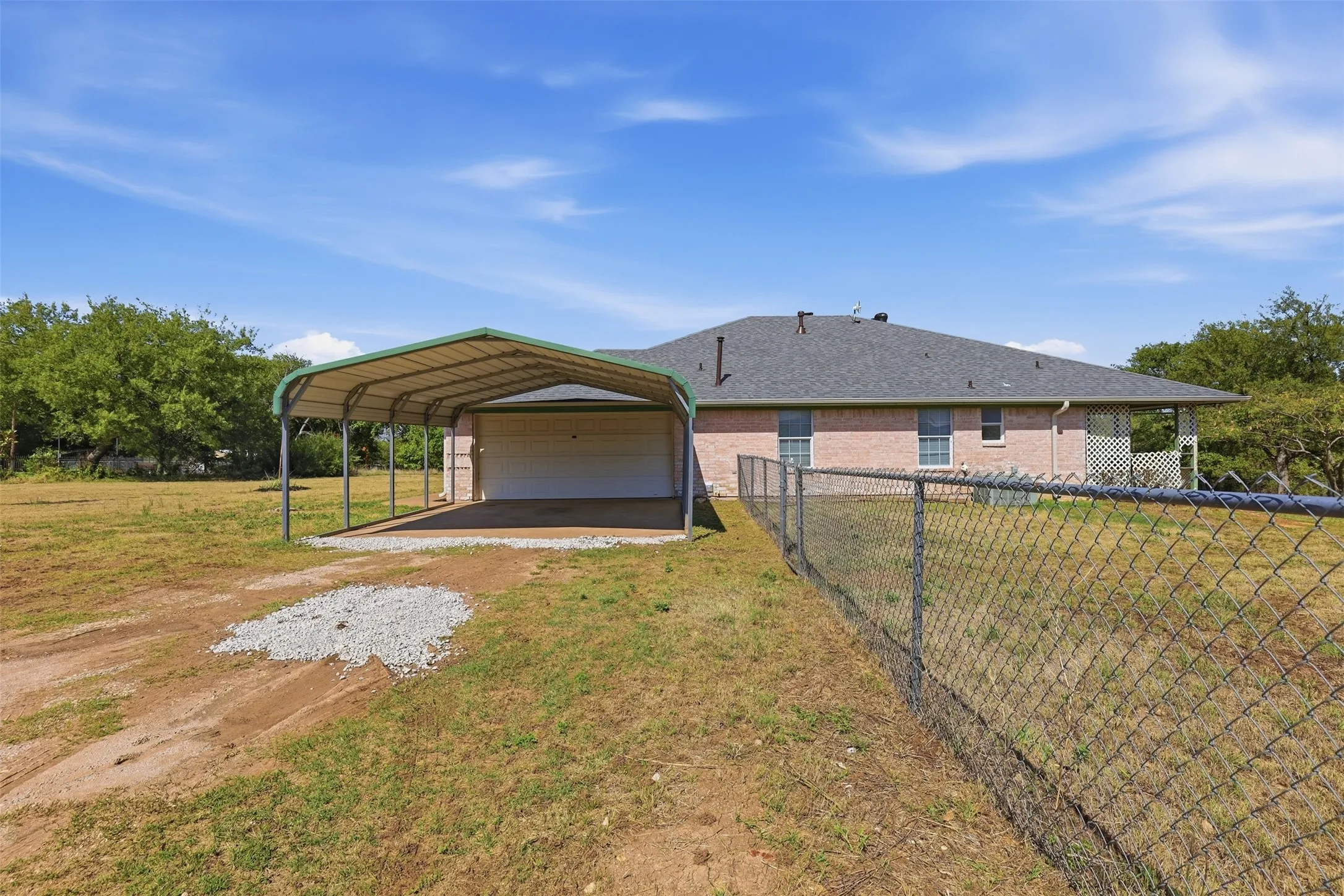 Attached carport structure, chain-link perimeter fencing, brick exterior, covered rear patio, and mature trees
