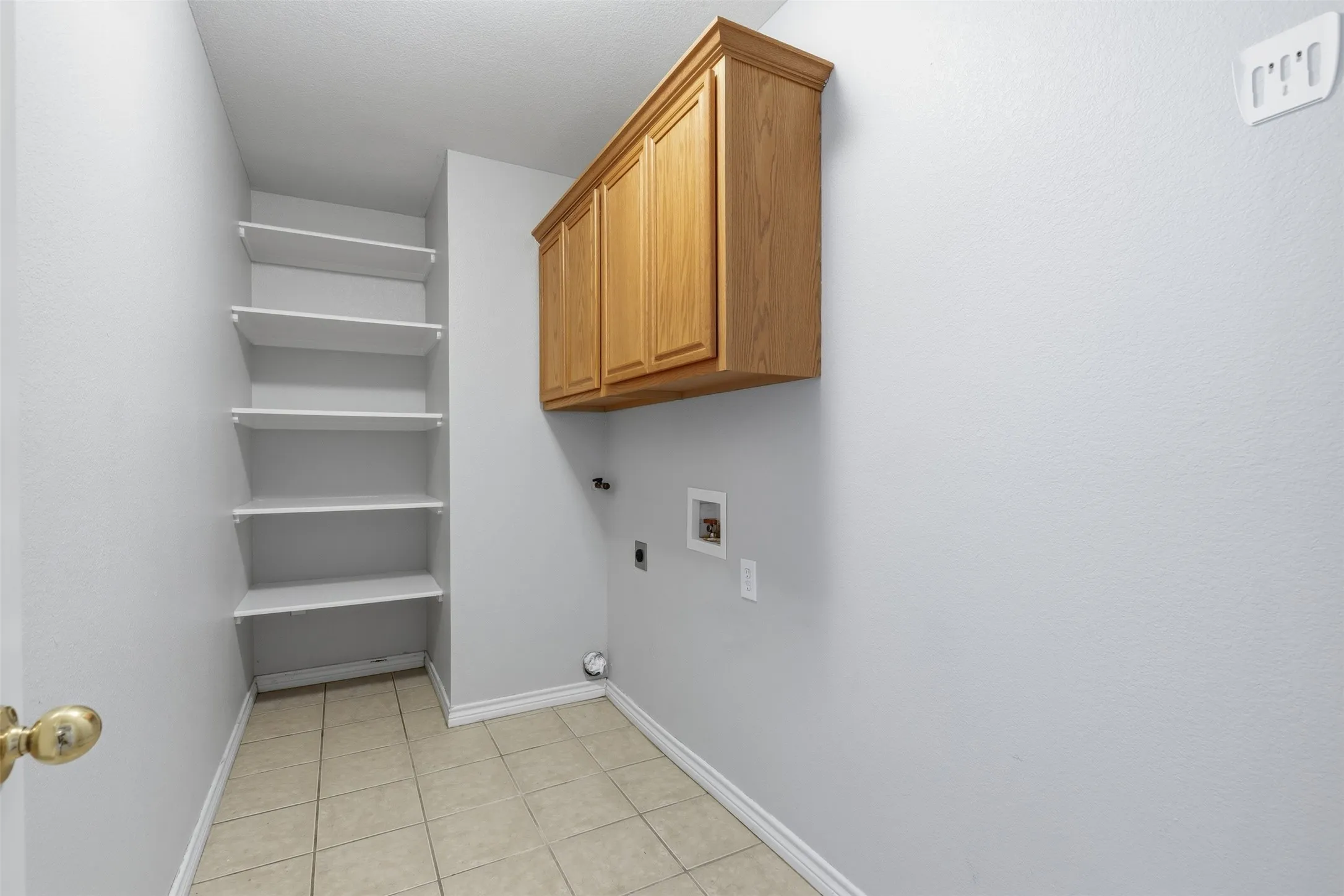 Utility room with tile flooring, built-in shelving, and wood-finish cabinetry