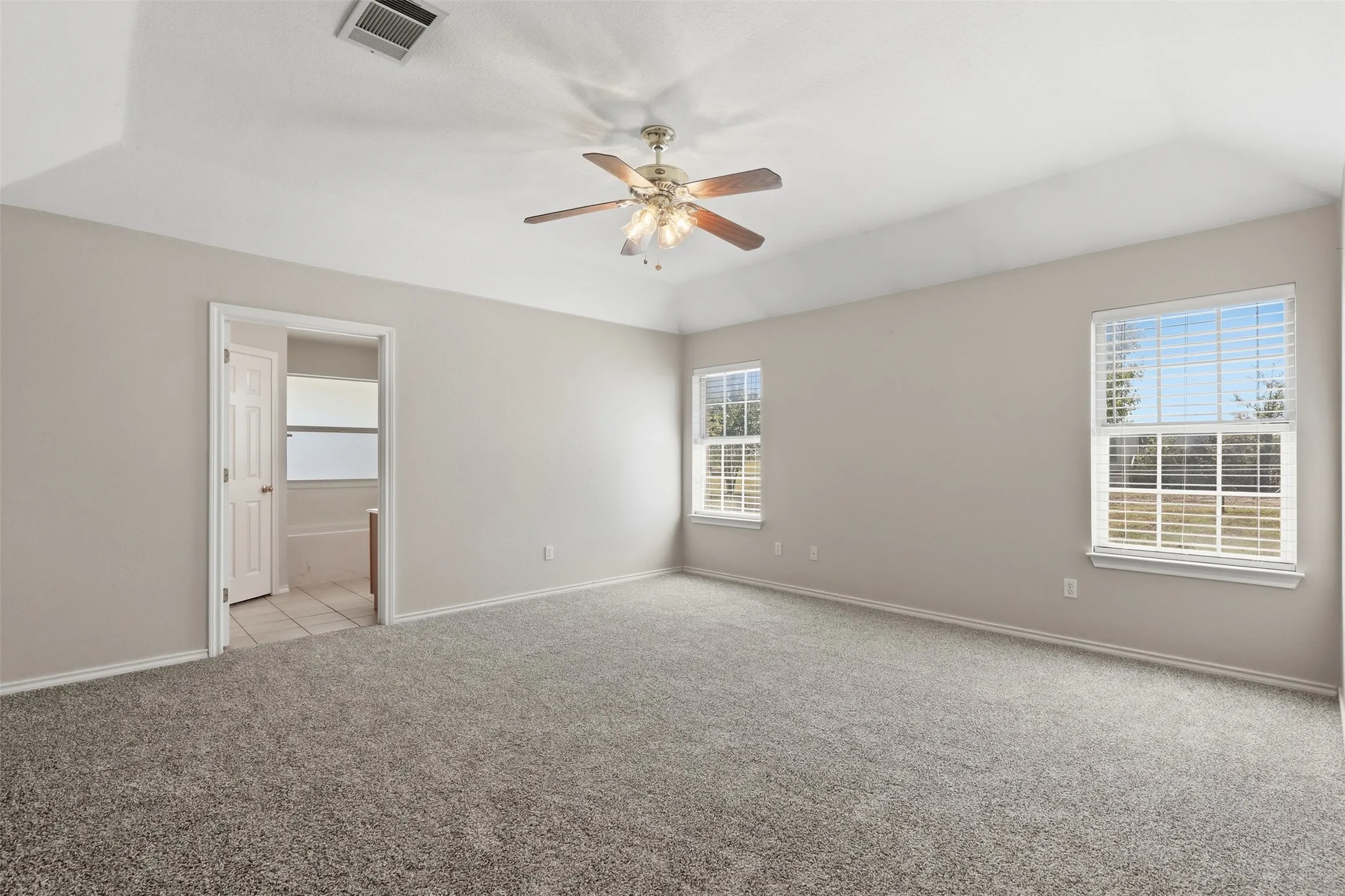 Vaulted ceiling with a ceiling fan, two double-hung windows, and wall-to-wall carpeting