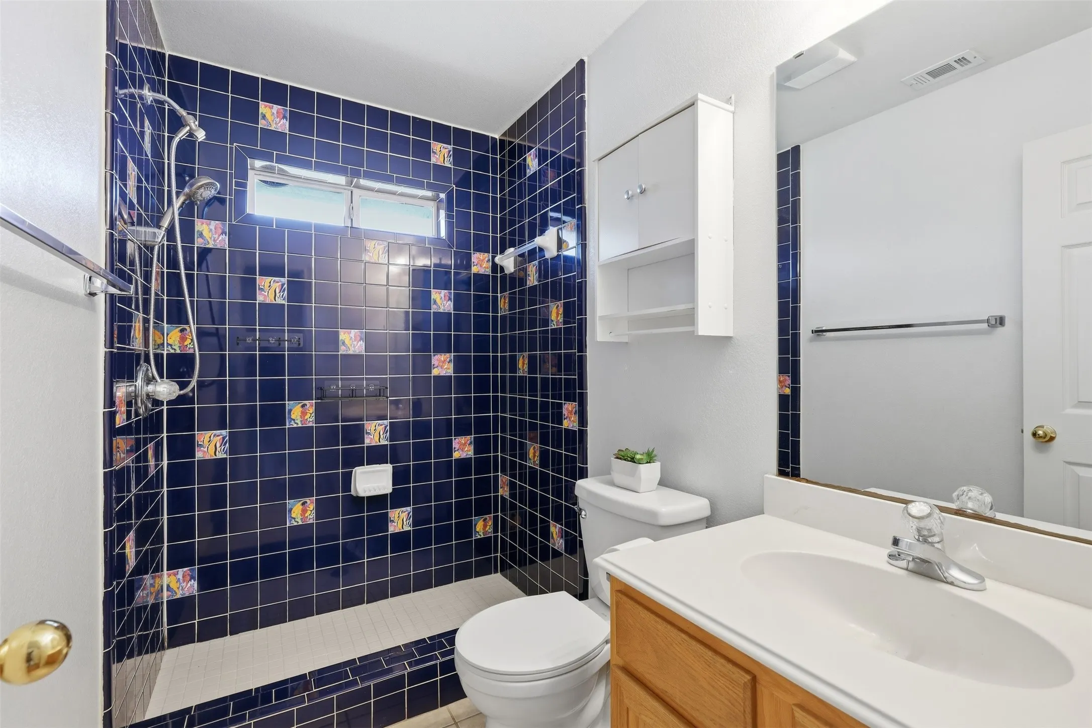 Full bathroom featuring a vanity with a white countertop and chrome faucet, a toilet, a built-in medicine cabinet, and a tiled shower with a window