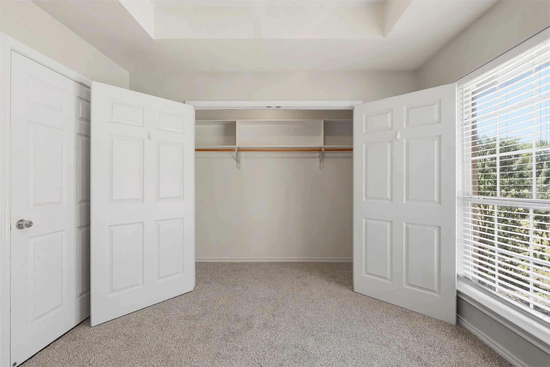 Recessed ceiling, light-toned carpeting, white six-panel doors, built-in closet shelving, and a window with blinds