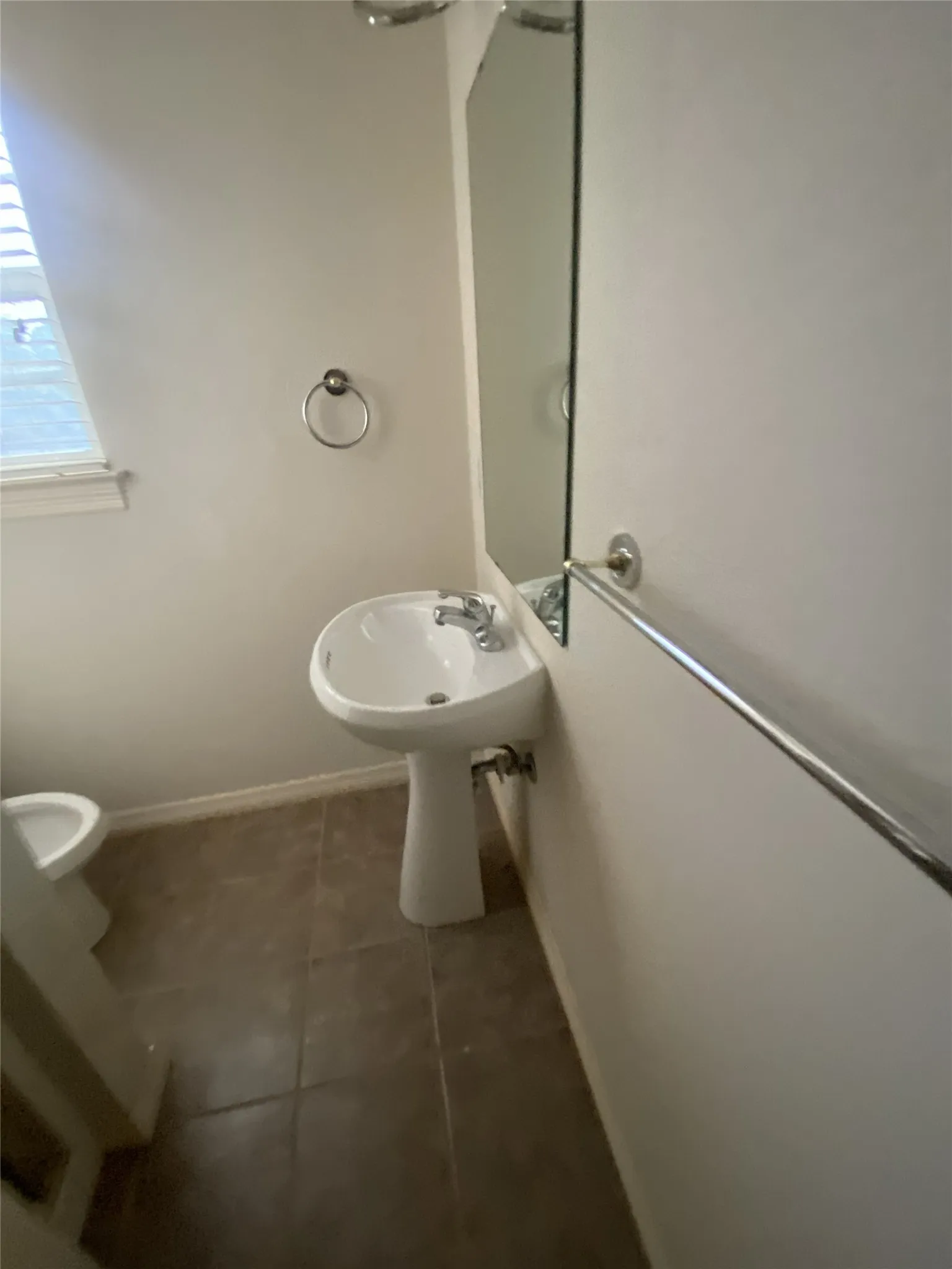 Pedestal sink with chrome faucet, mirror, wall-mounted towel bar, and tile flooring